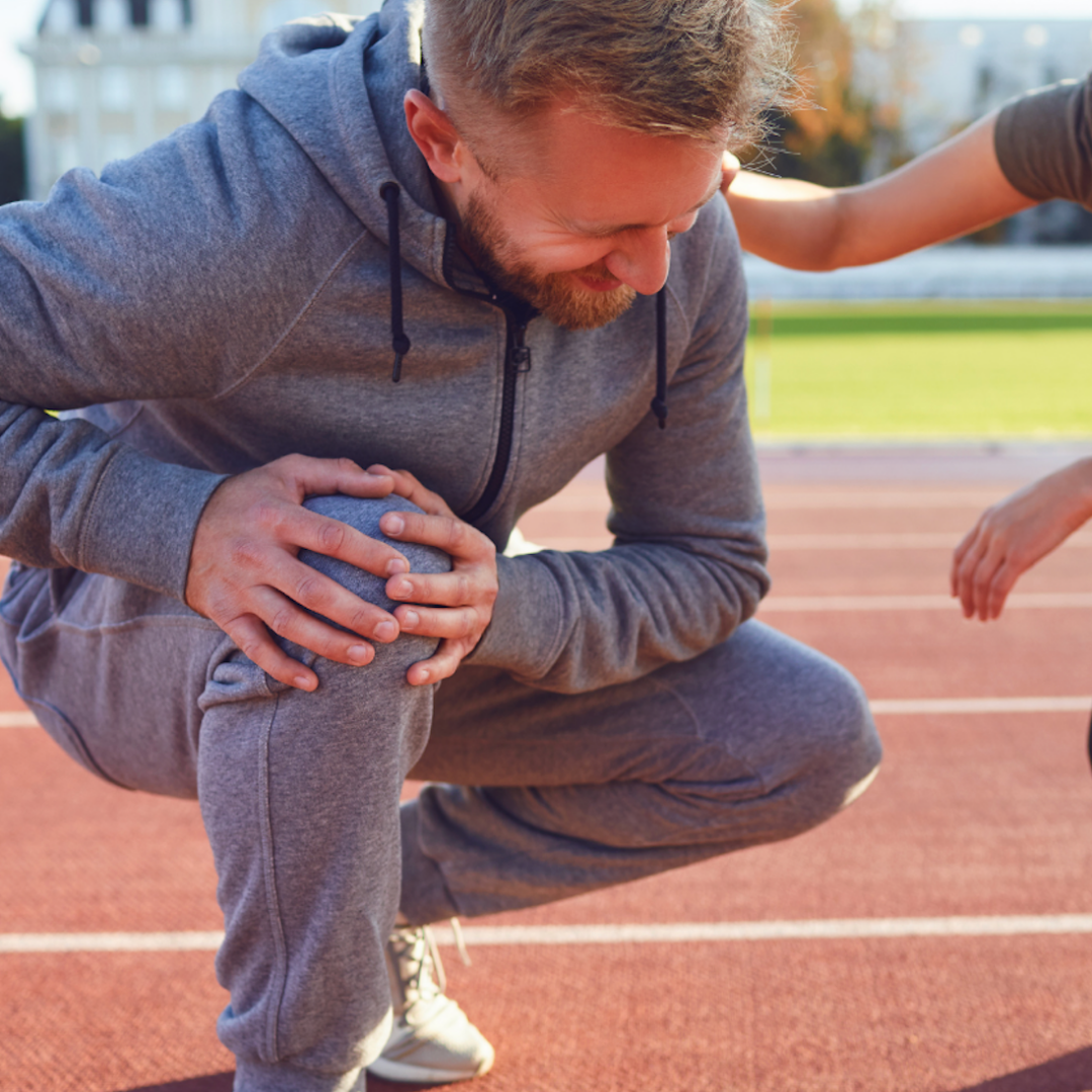 Middle-aged man hurt over ACL injury on a running track.