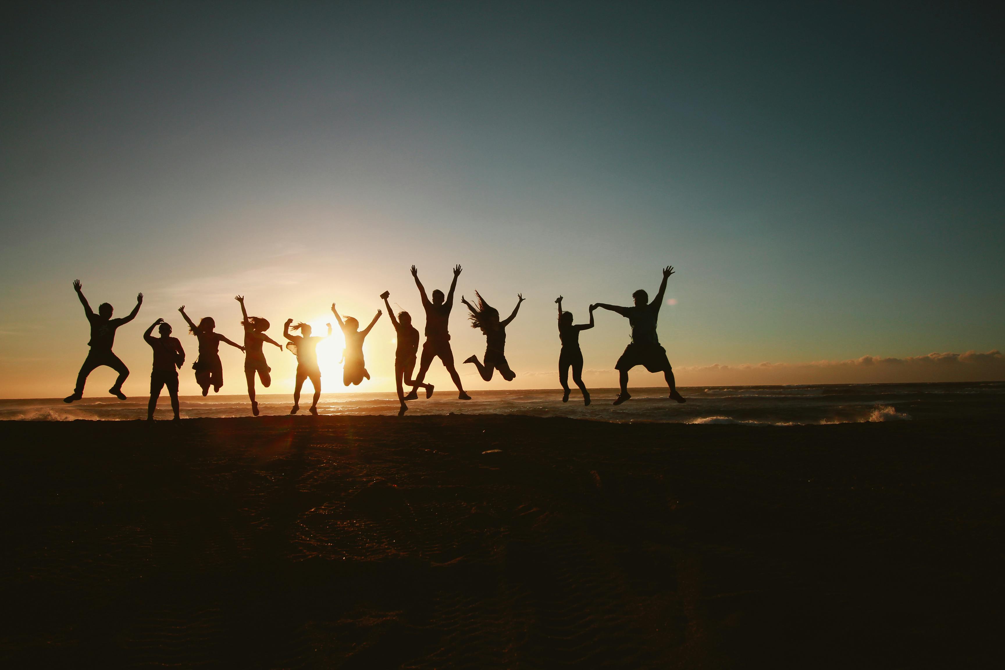 happy group of people jumping at the seashore at sunset