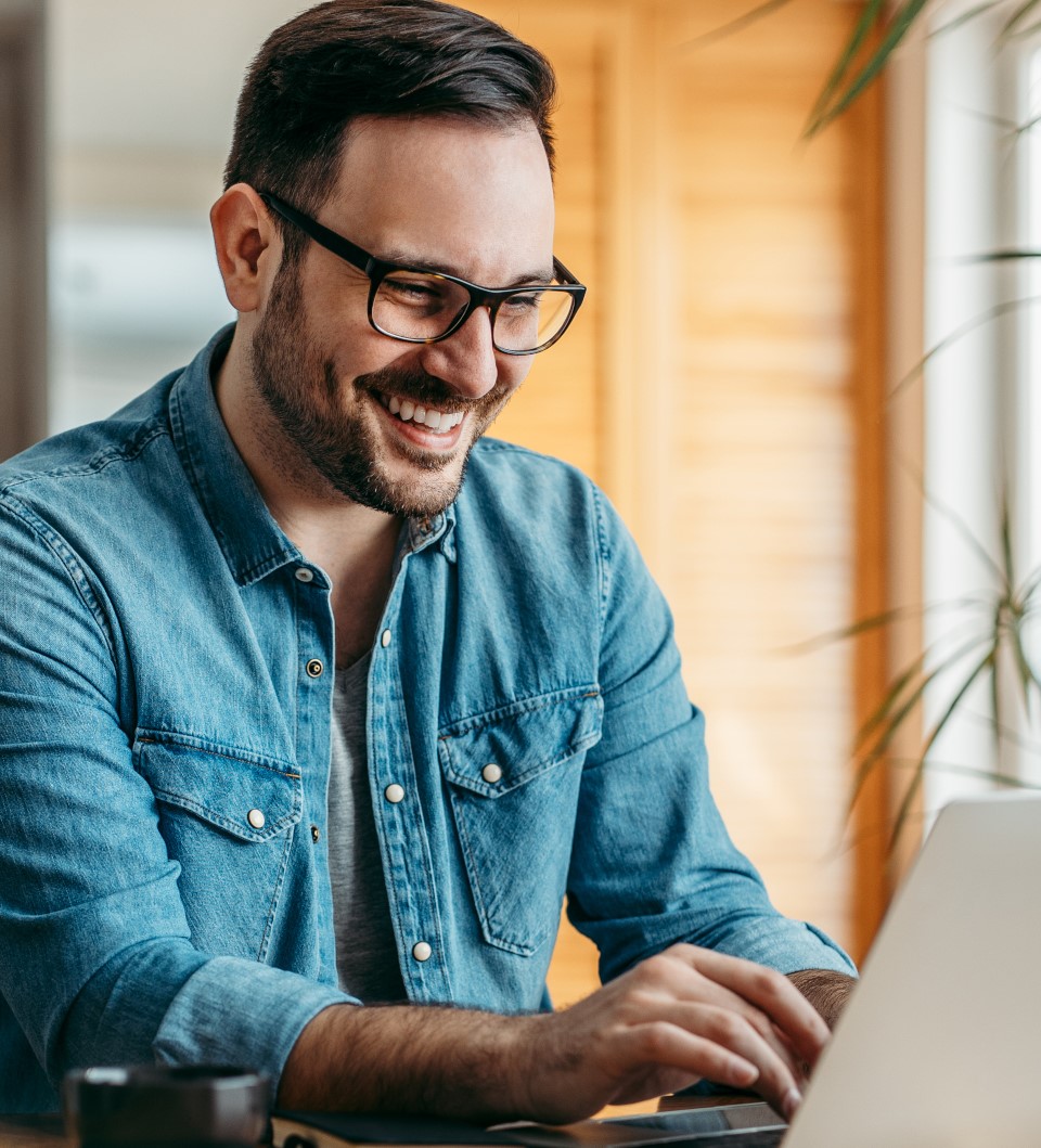 Ein Mann, der an seinem Laptop arbeitet und lacht