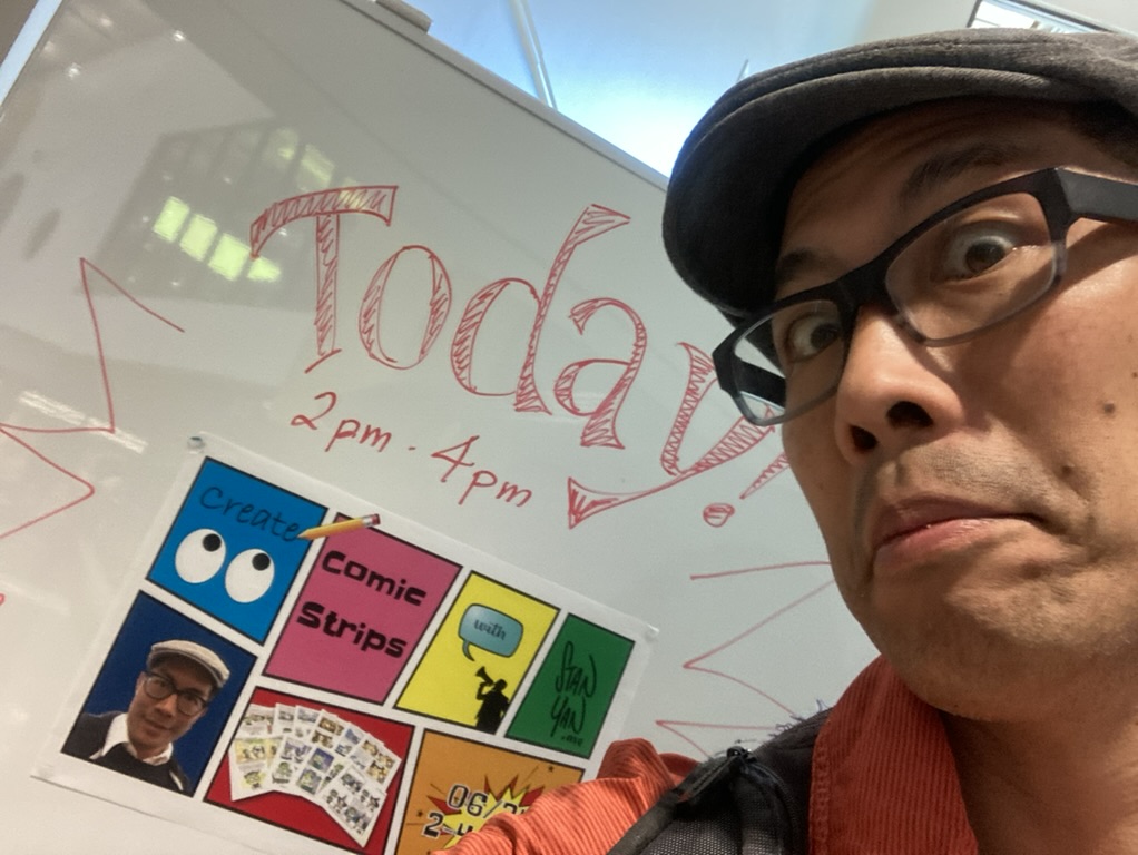 Stan Yan posing in front of a comic strip workshop sign