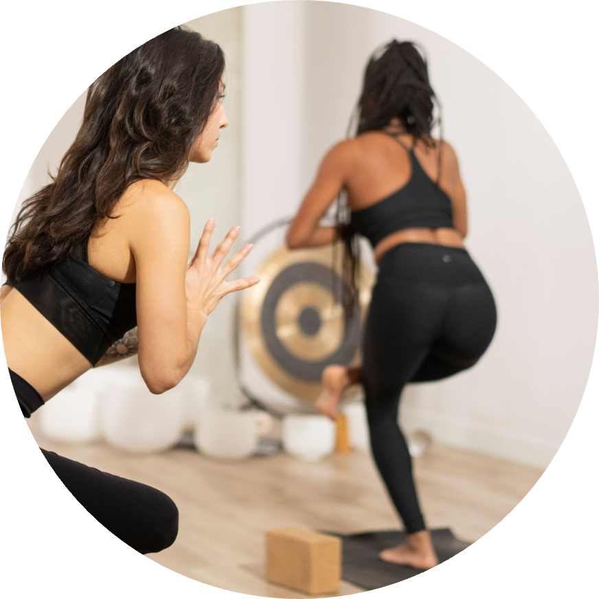 Two yogis in chair pose in a yoga studio with a gong and crystal bowls