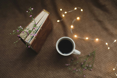 A coffee cup next to fairy lights and a notebook with flowers between the pages