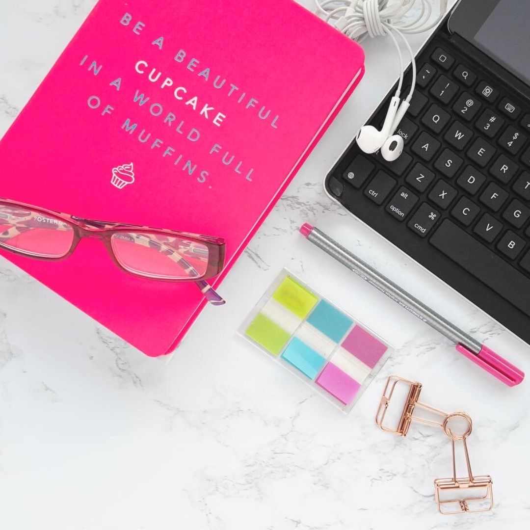 flatlay photography with pink notebook, Pink pen, pink reading glasses, keyboard, earbuds, stickies and gold clips