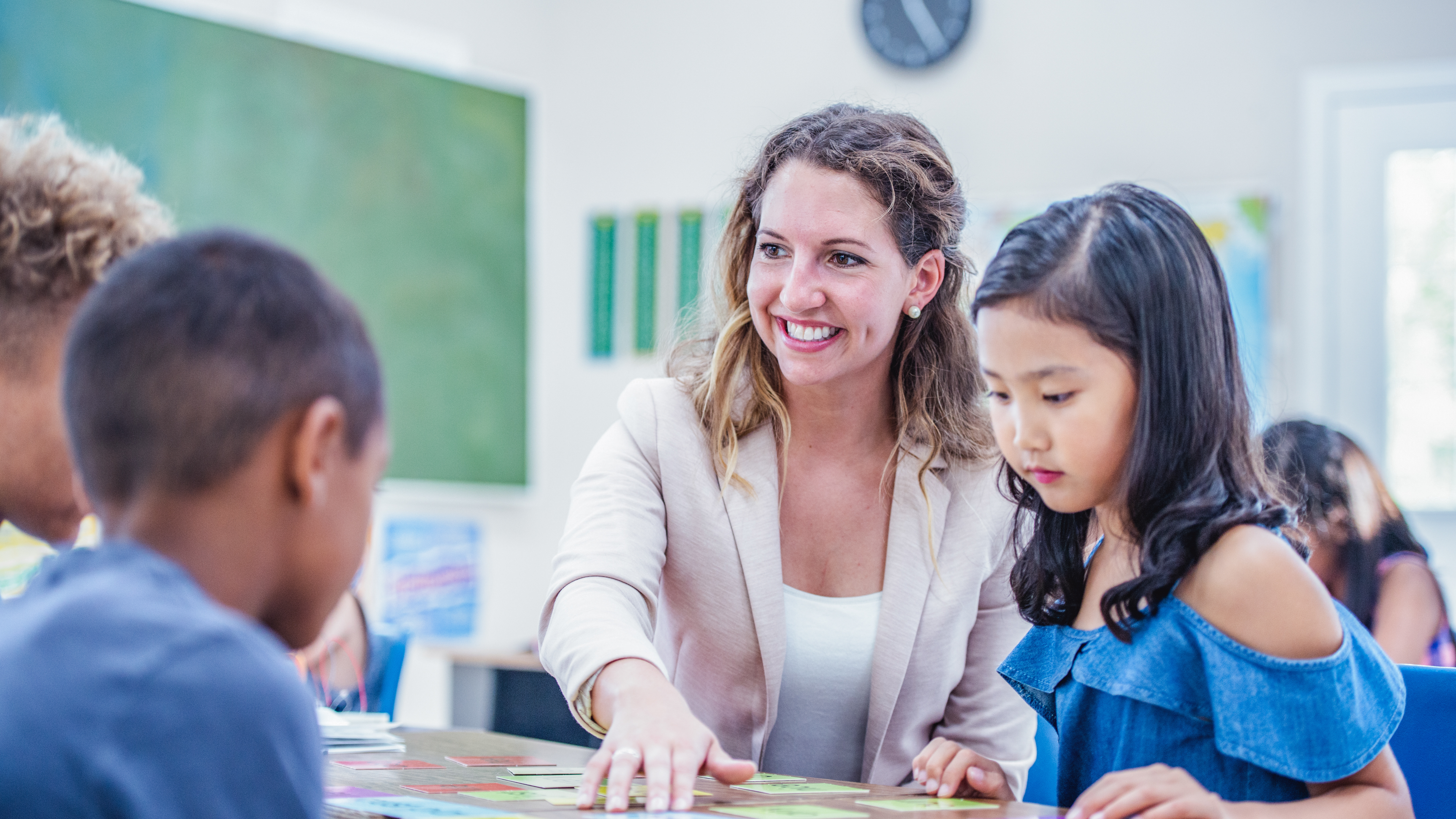 teacher smiling working at a table with students and flashcards