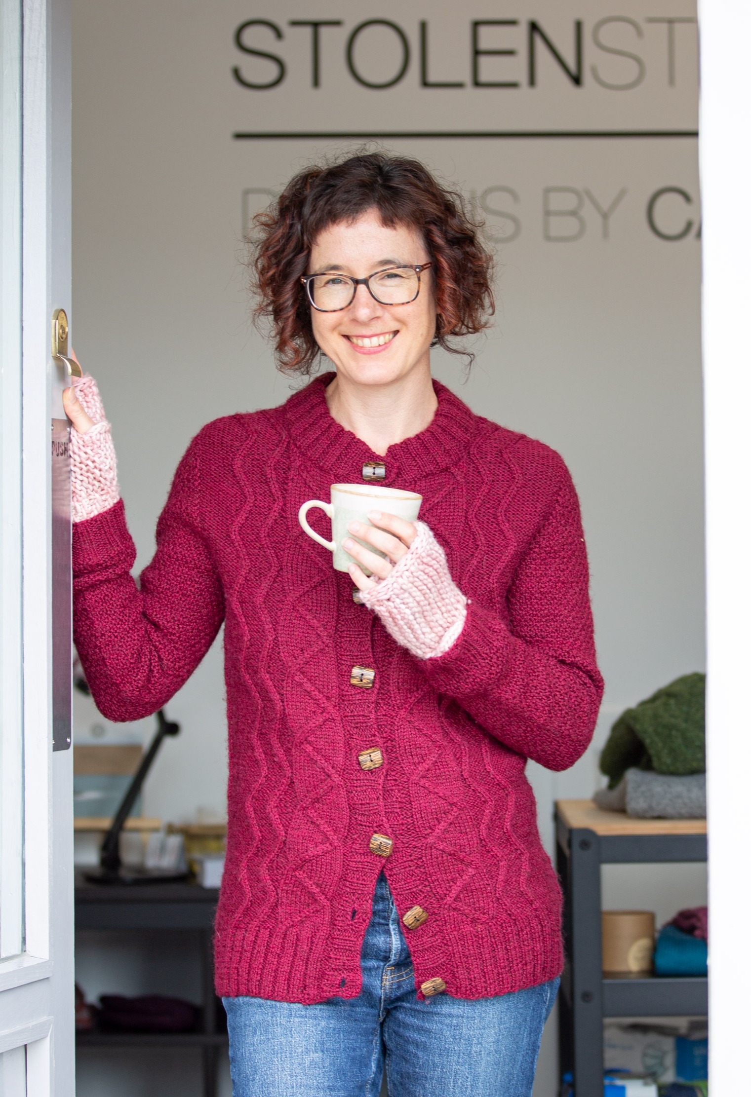 Carol Feller standing in the doorway of the Stolen Stitches shop in Cork holdaing a cup of coffee and smiling at the camera.