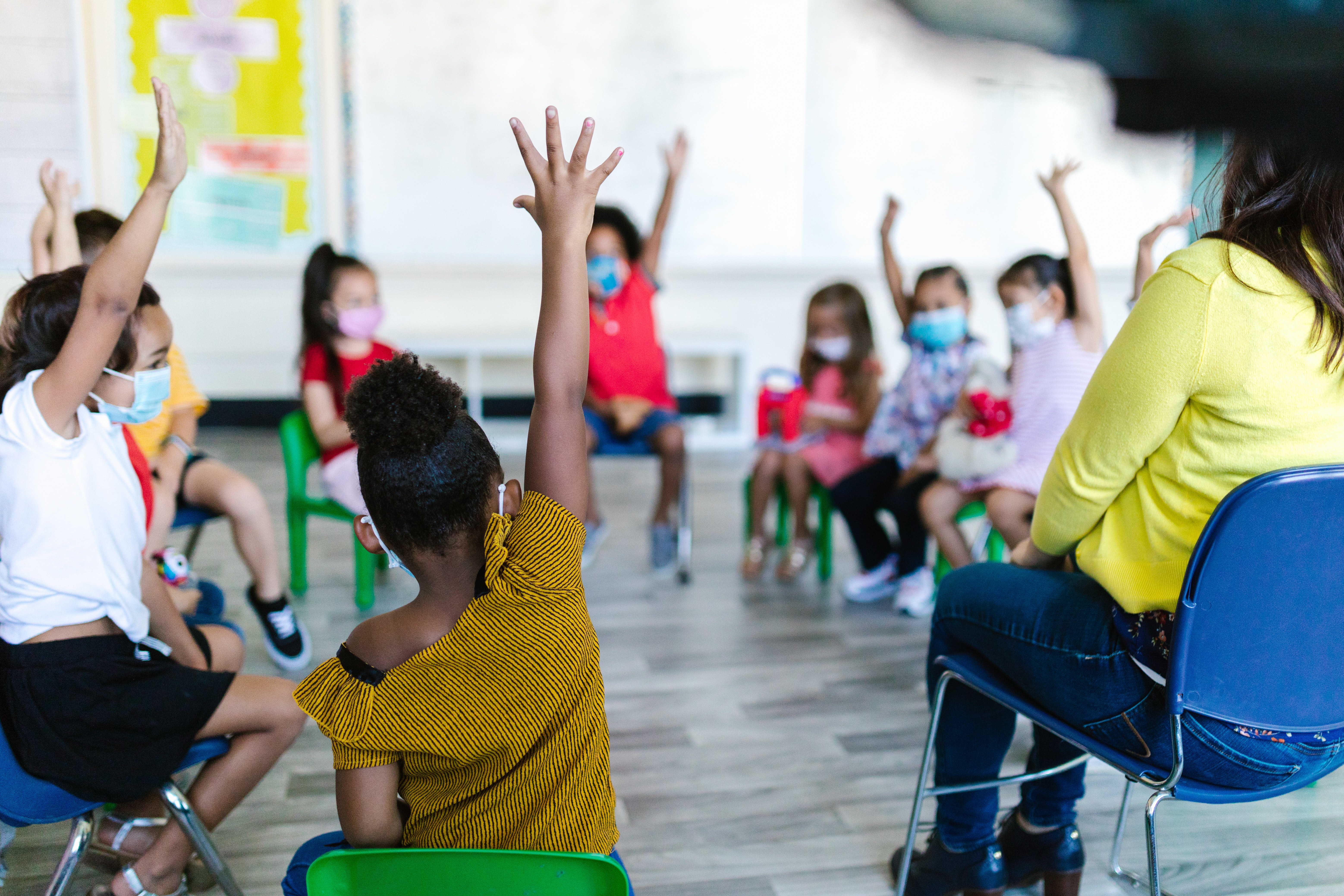 children sitting in circle with hands raised