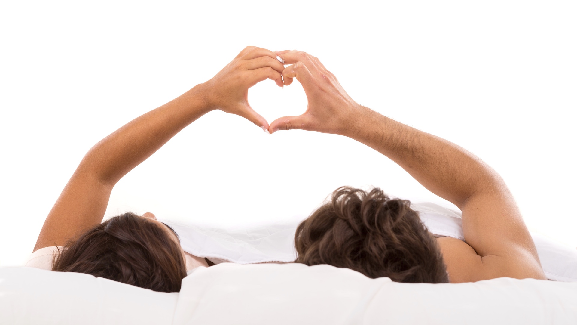 Married couple in bed making a heart sign with their hands