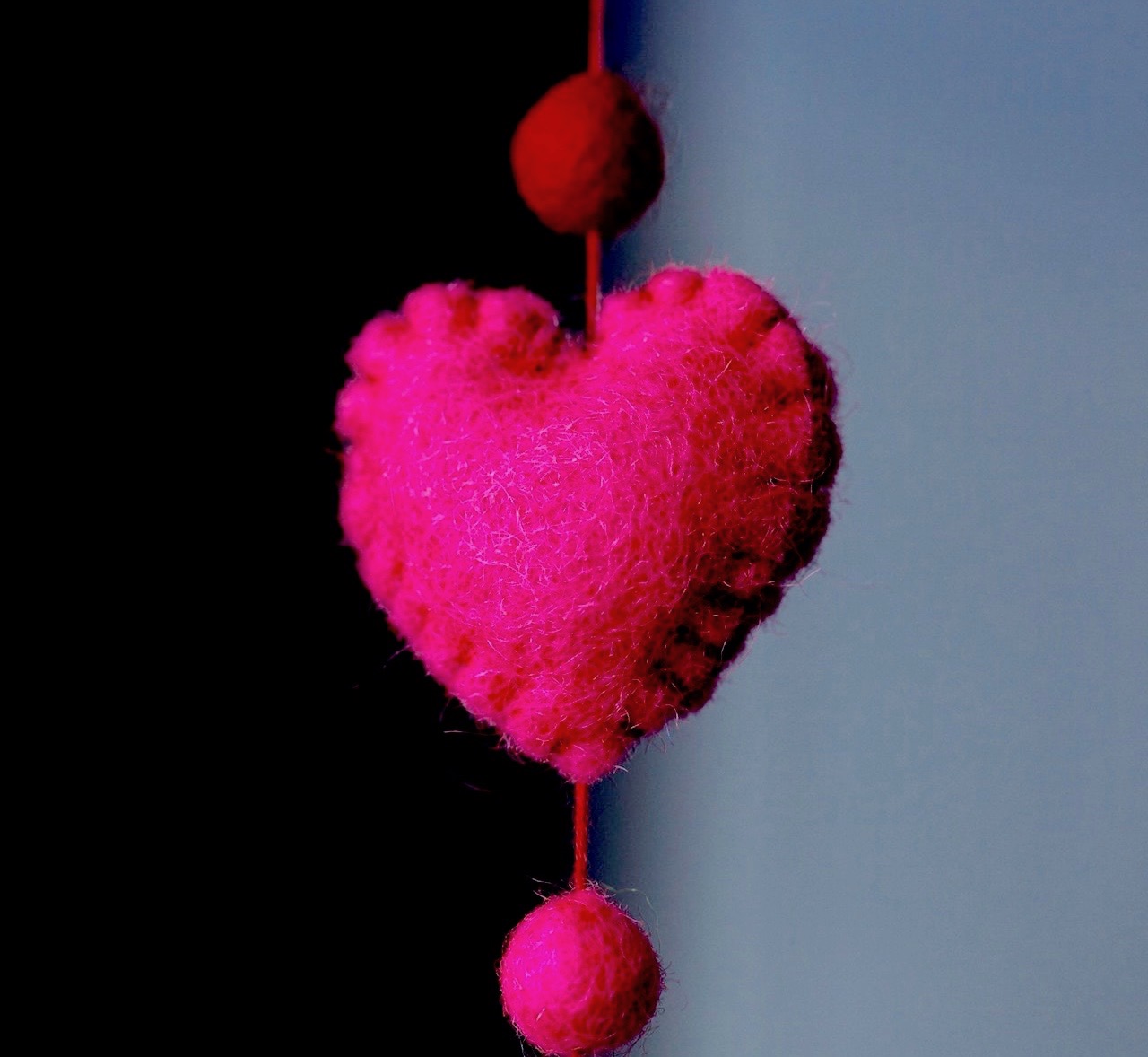 Fuschia pink heart made of felt hanging against a dark background
