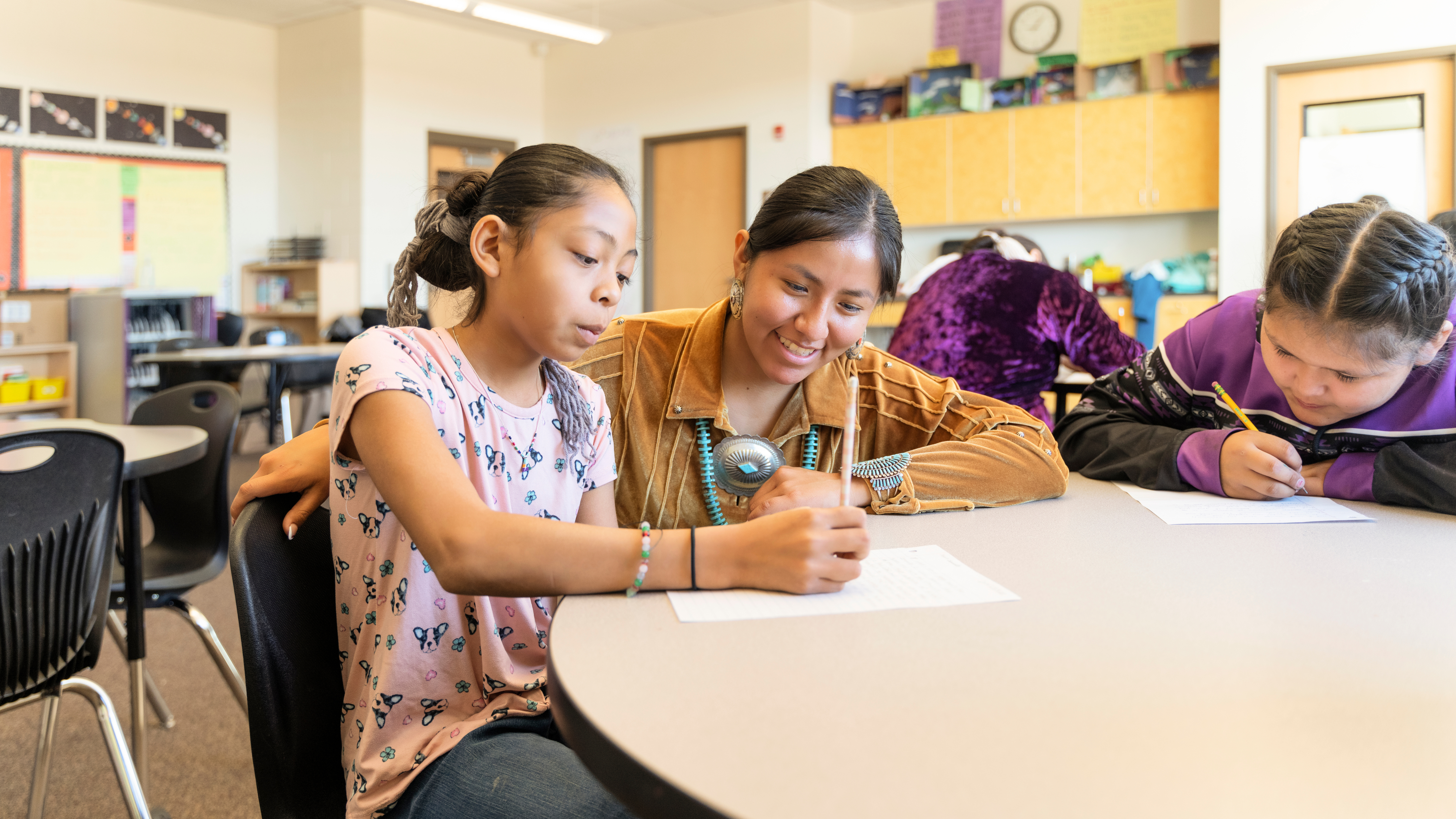 teacher helping student writing at table