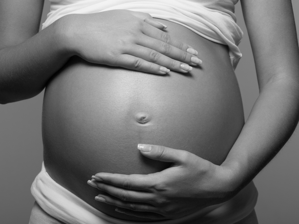 close up of bare pregnant belly with hands on the top and bottom