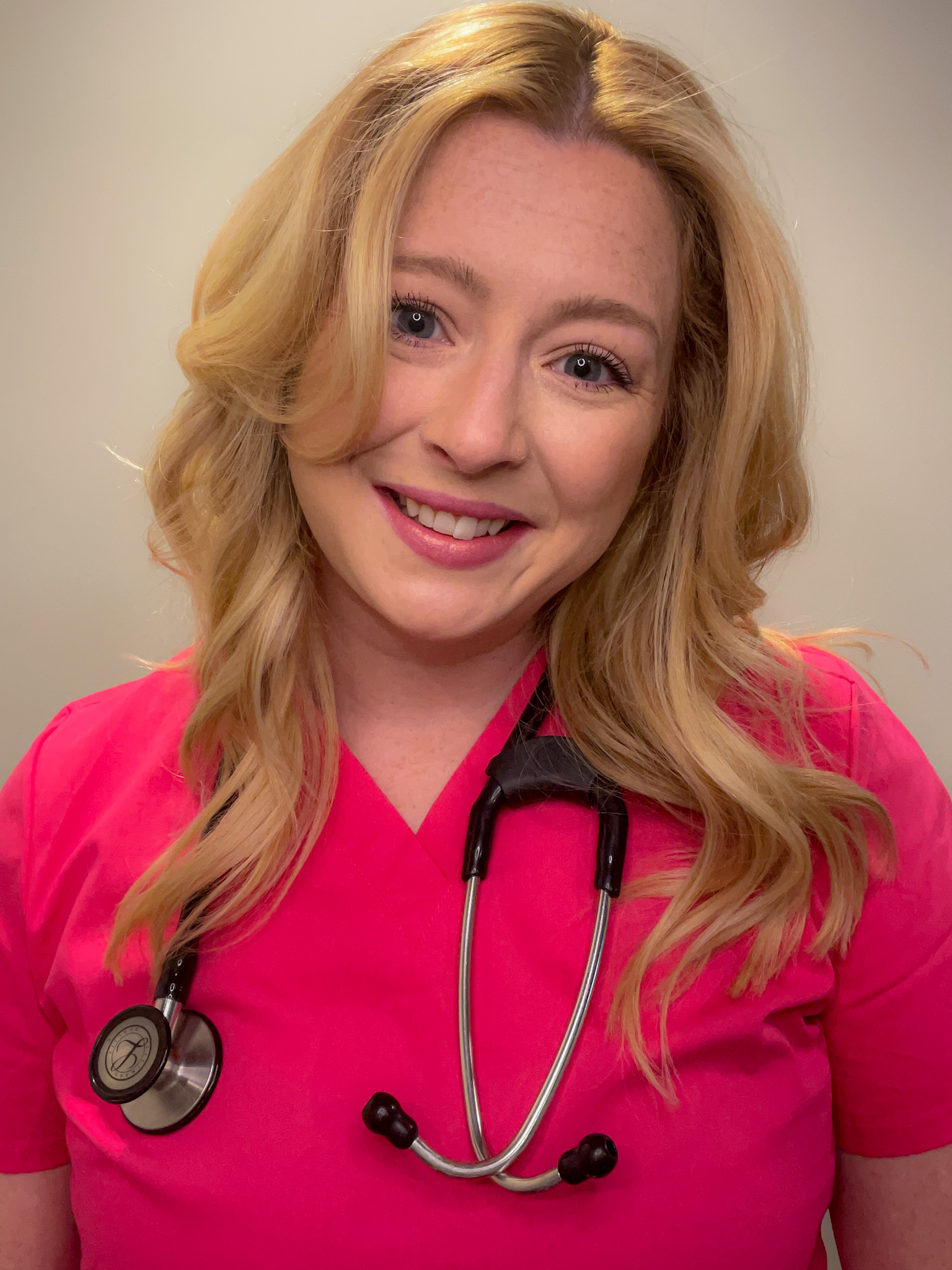 lindsey a blonde nurse wearing pink scrubs with curly hair smiling