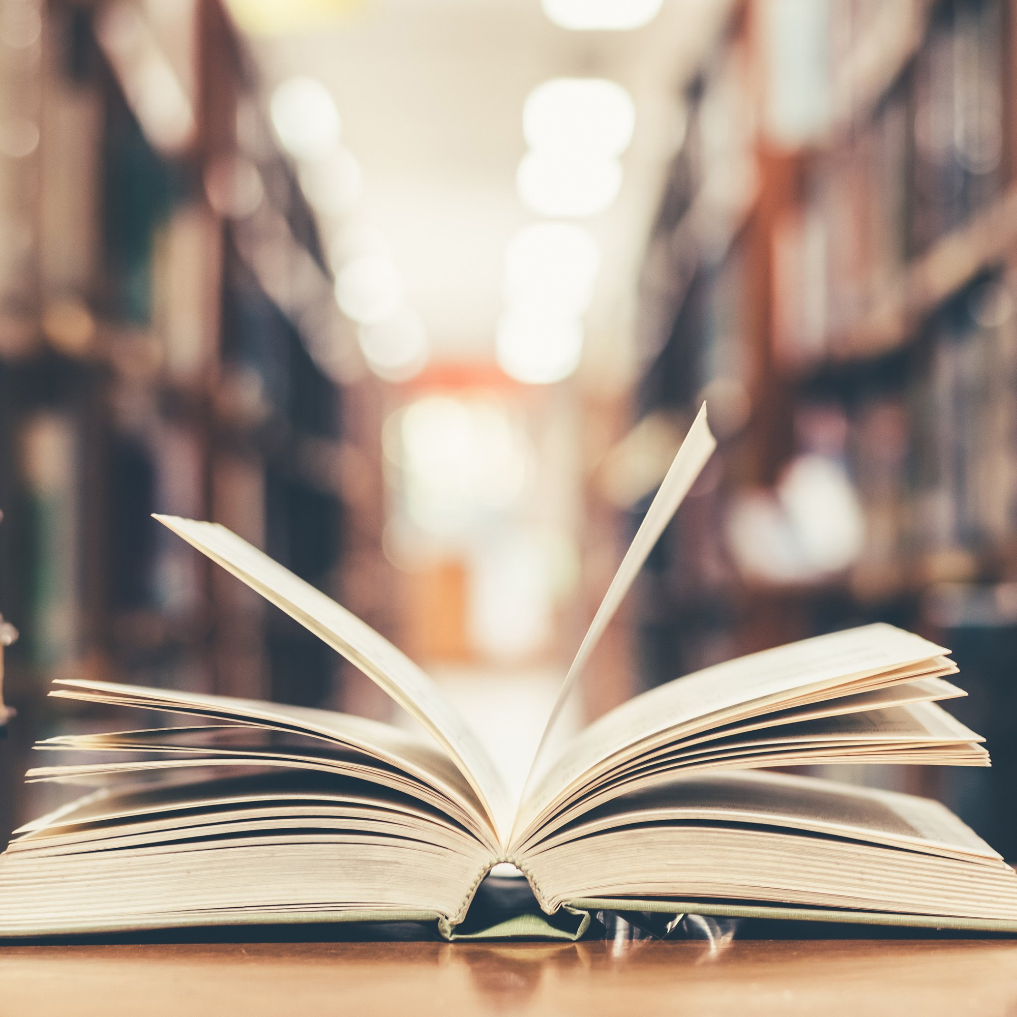 An open book in the foreground, bookshelves in the background