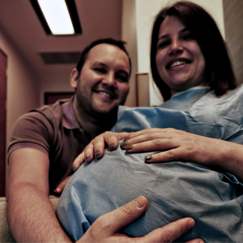 pregnant woman smiling holding belly with man behind her smiling