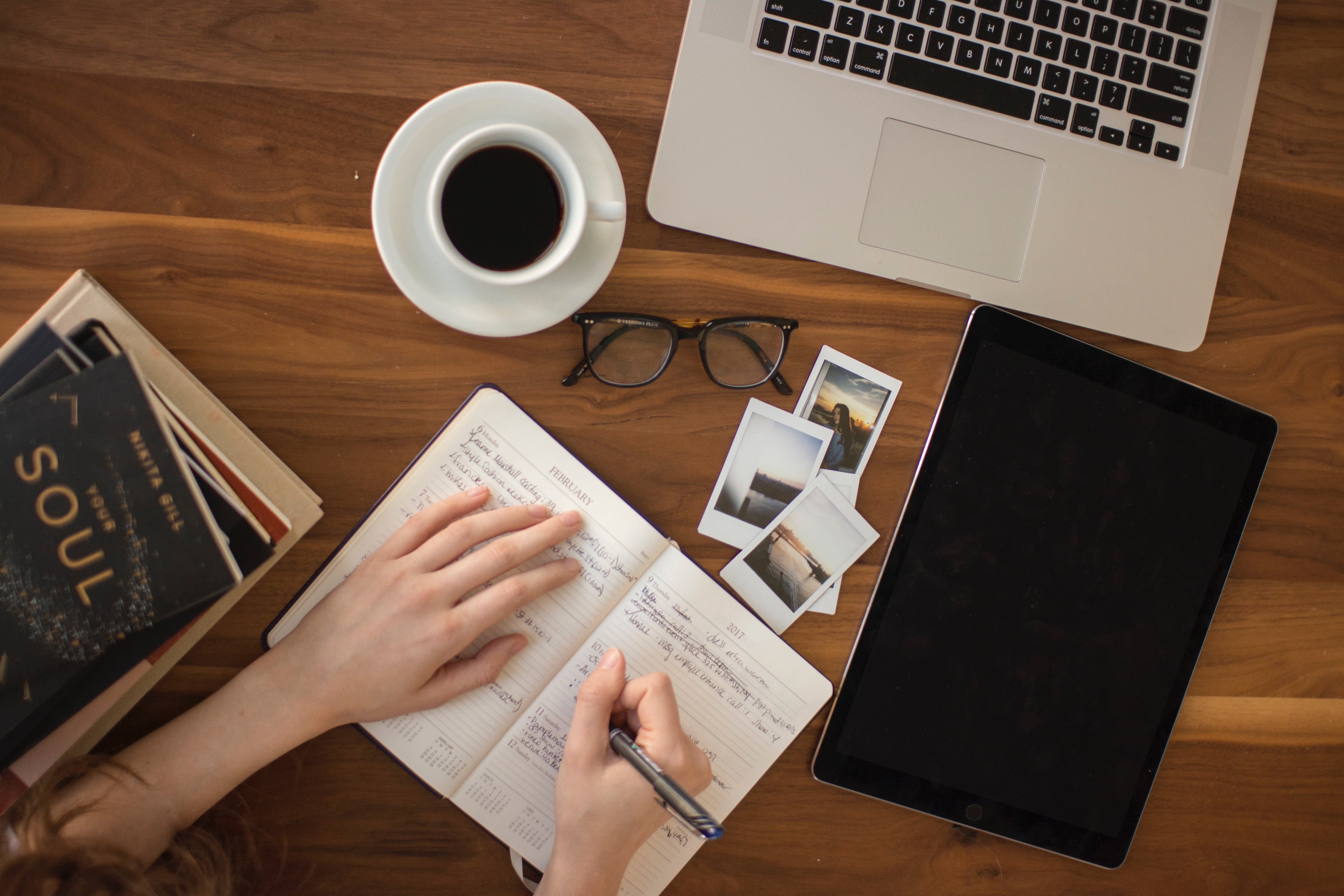 Student hand writing college essay application on paper in front of a laptop