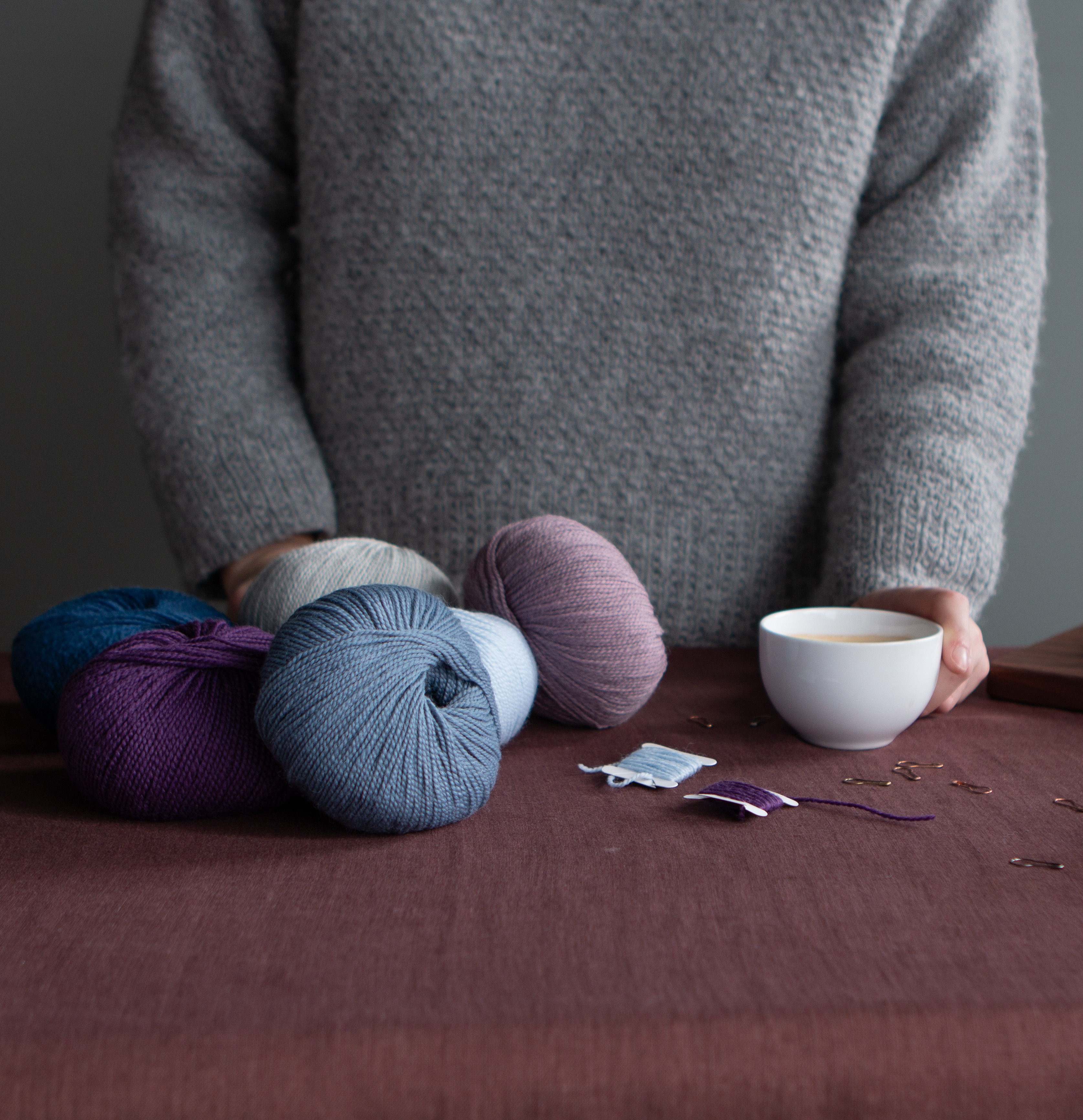 Image of desk with yarn and coffee and person stood behind. 