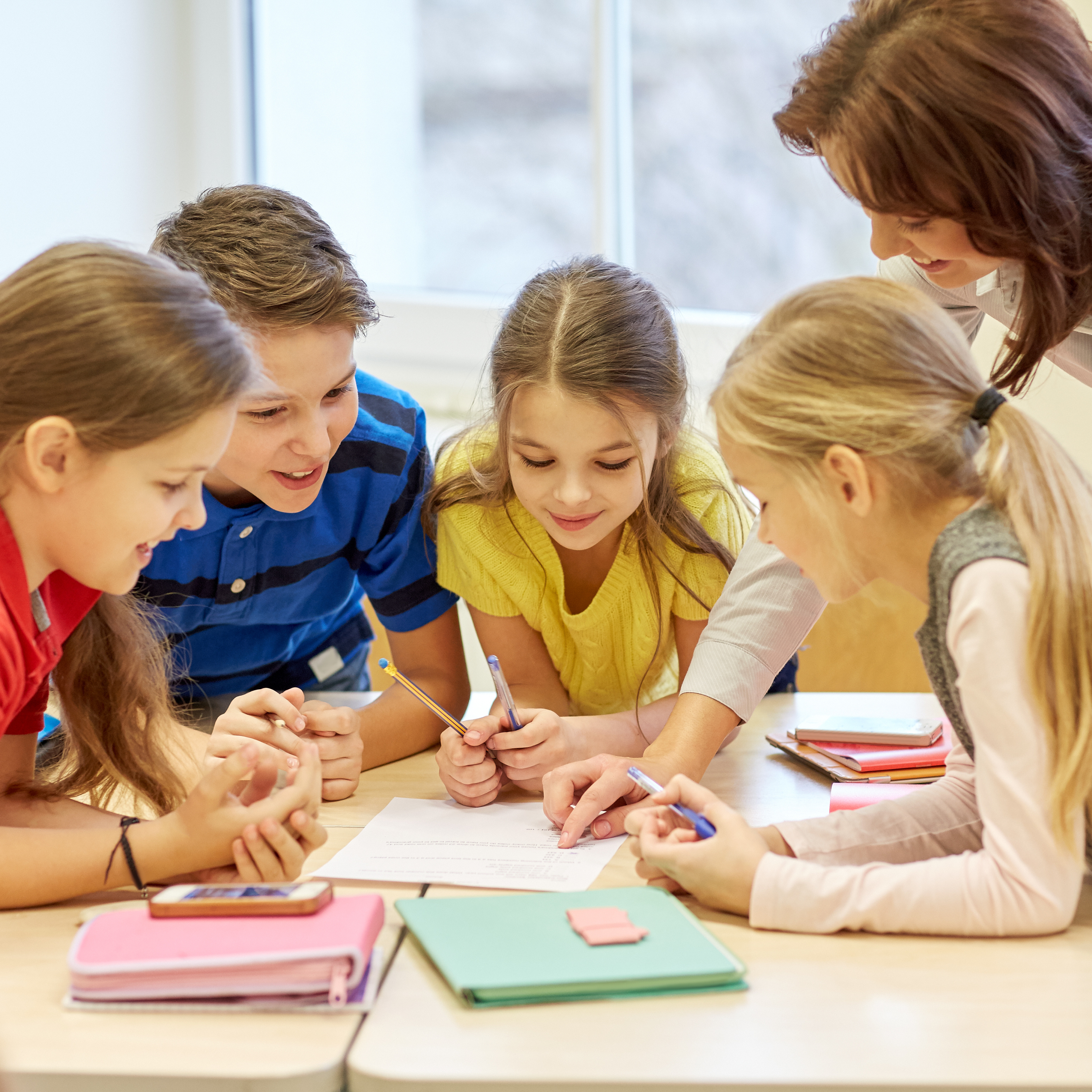 teacher working with students using writing tools on desk