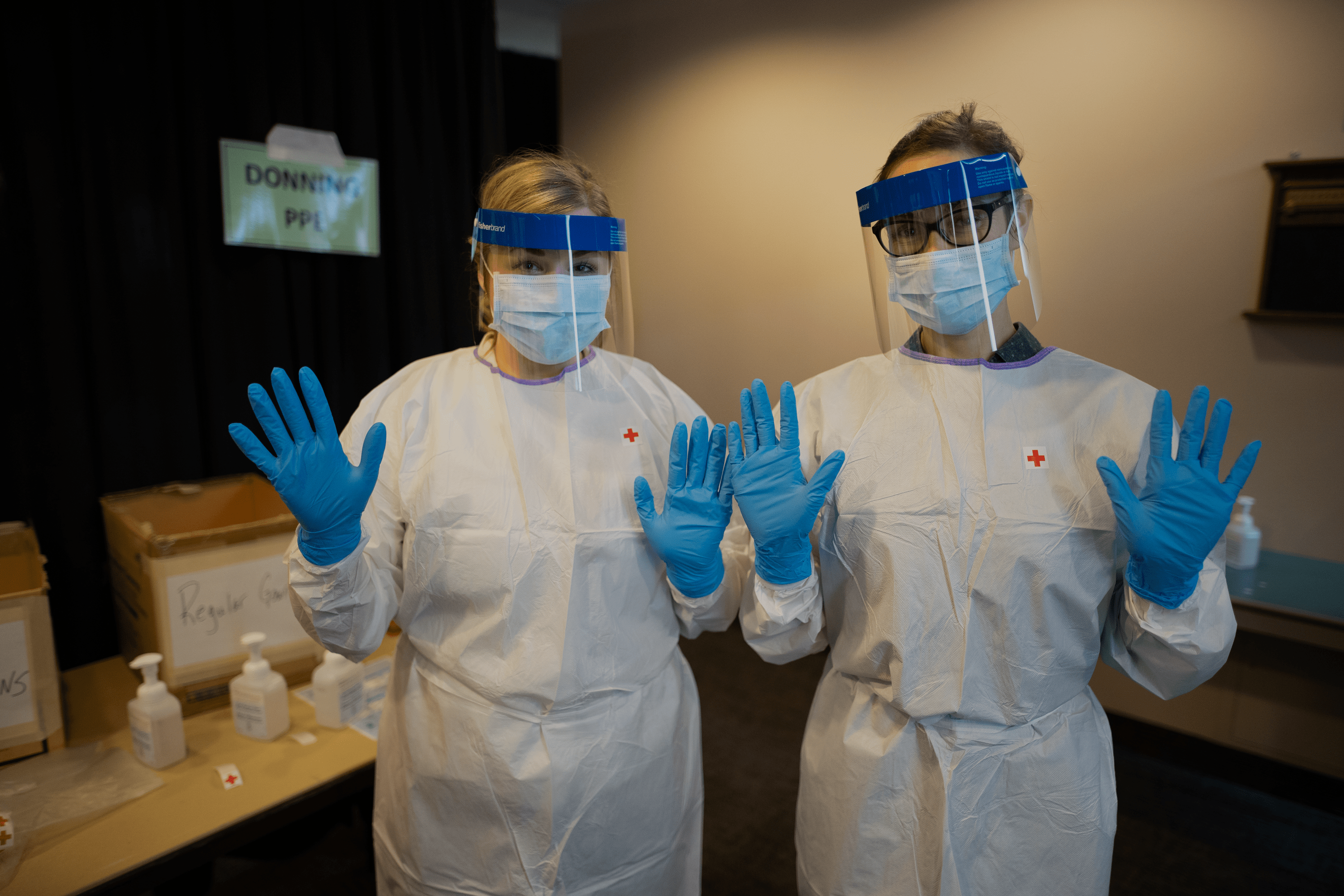 Two people standing next to each other wearing gloves, masks, and gowns for personal protective equipment.