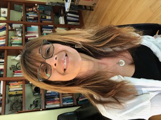Image of Darlene Easton, long hair, dark framed glasses, wearing a white shirt in a room with a large book shelf.