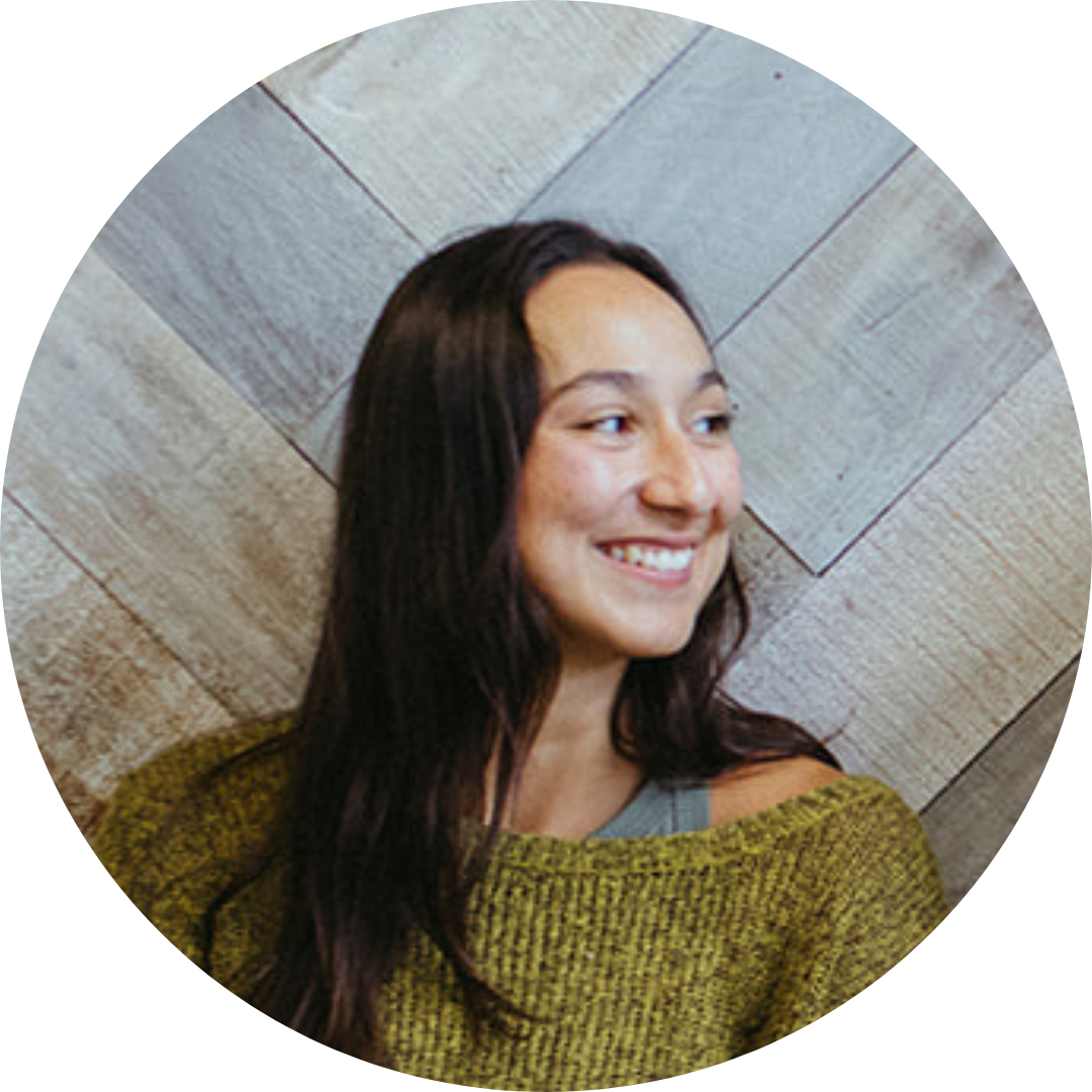 A photo of Alex wearing a green sweater smiling and looking to the right