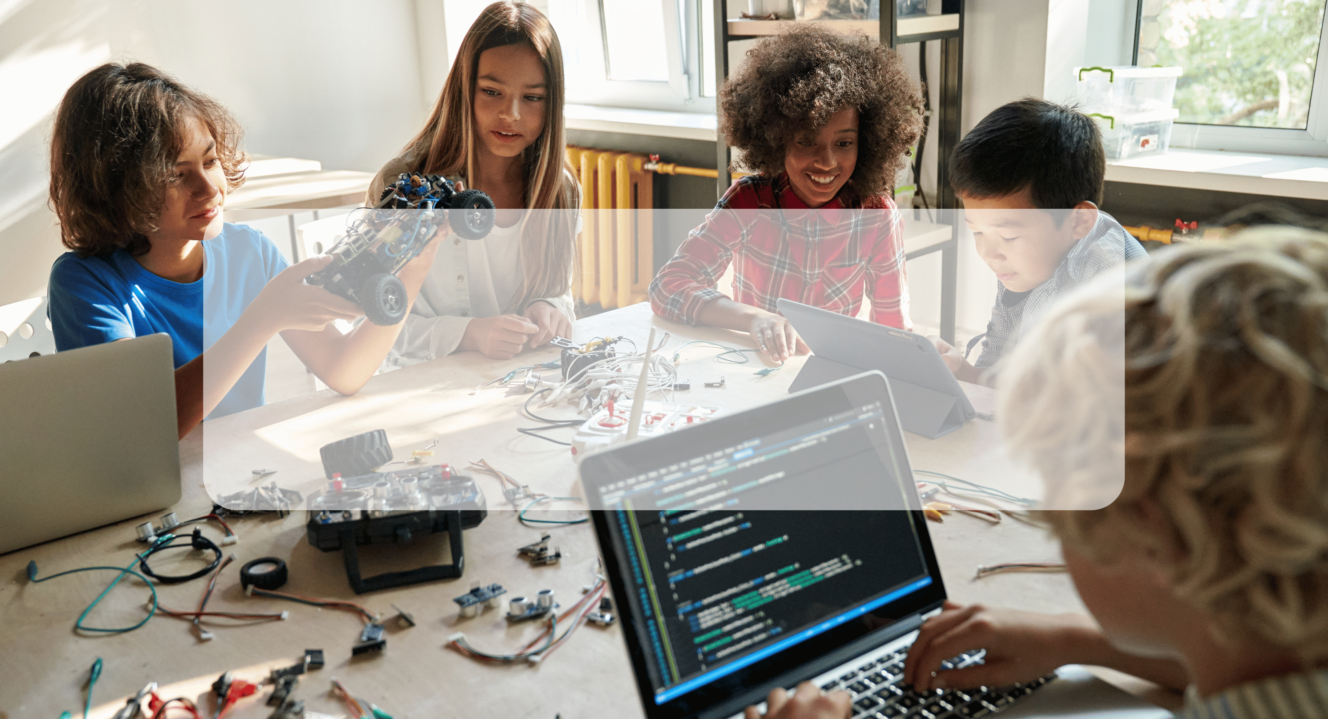 students coding collaboratively at a table with equipment and a laptop