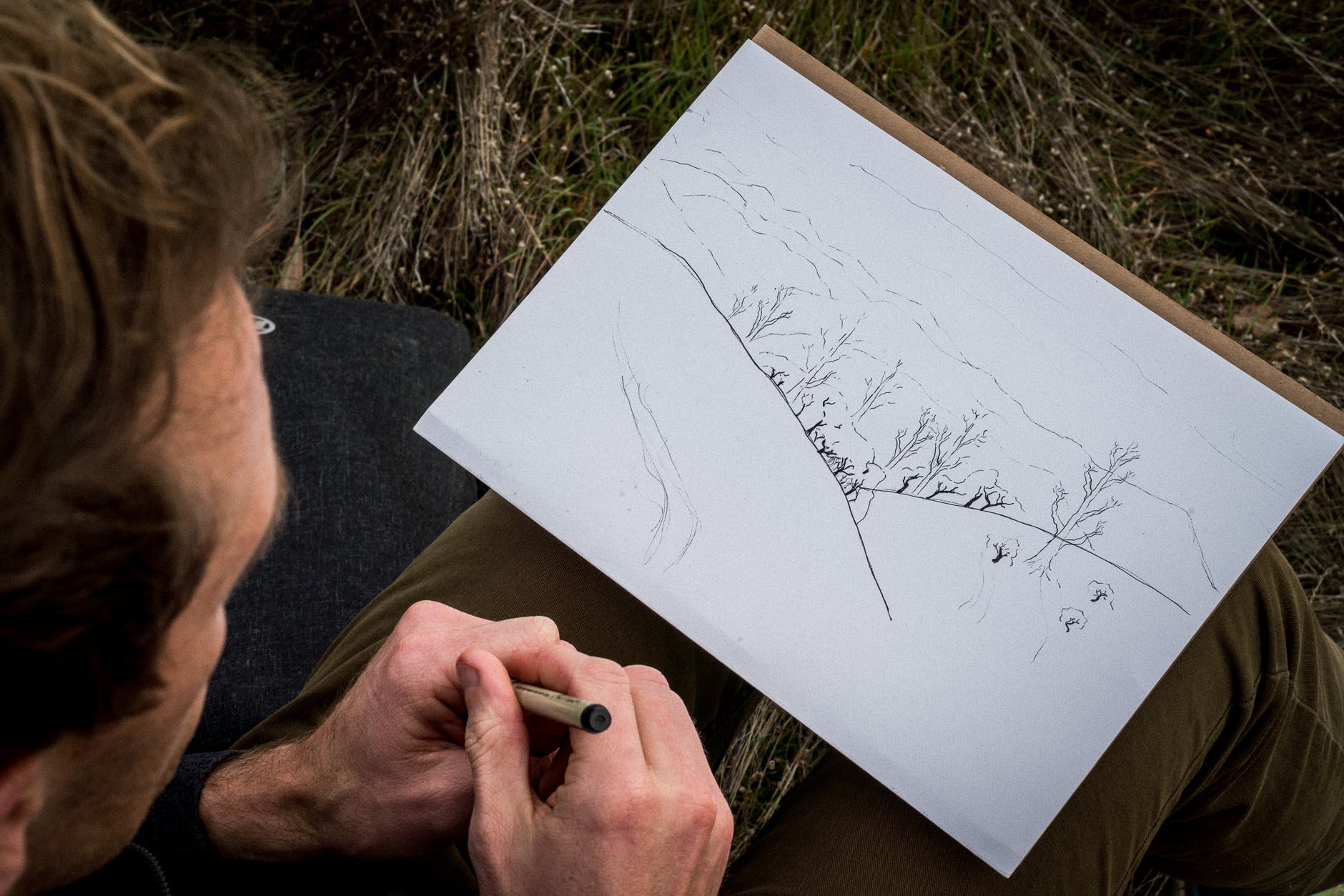 Man looking at his drawing of the landscape while sitting outside