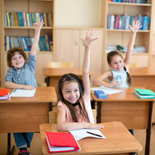 Children in classroom with their hands up