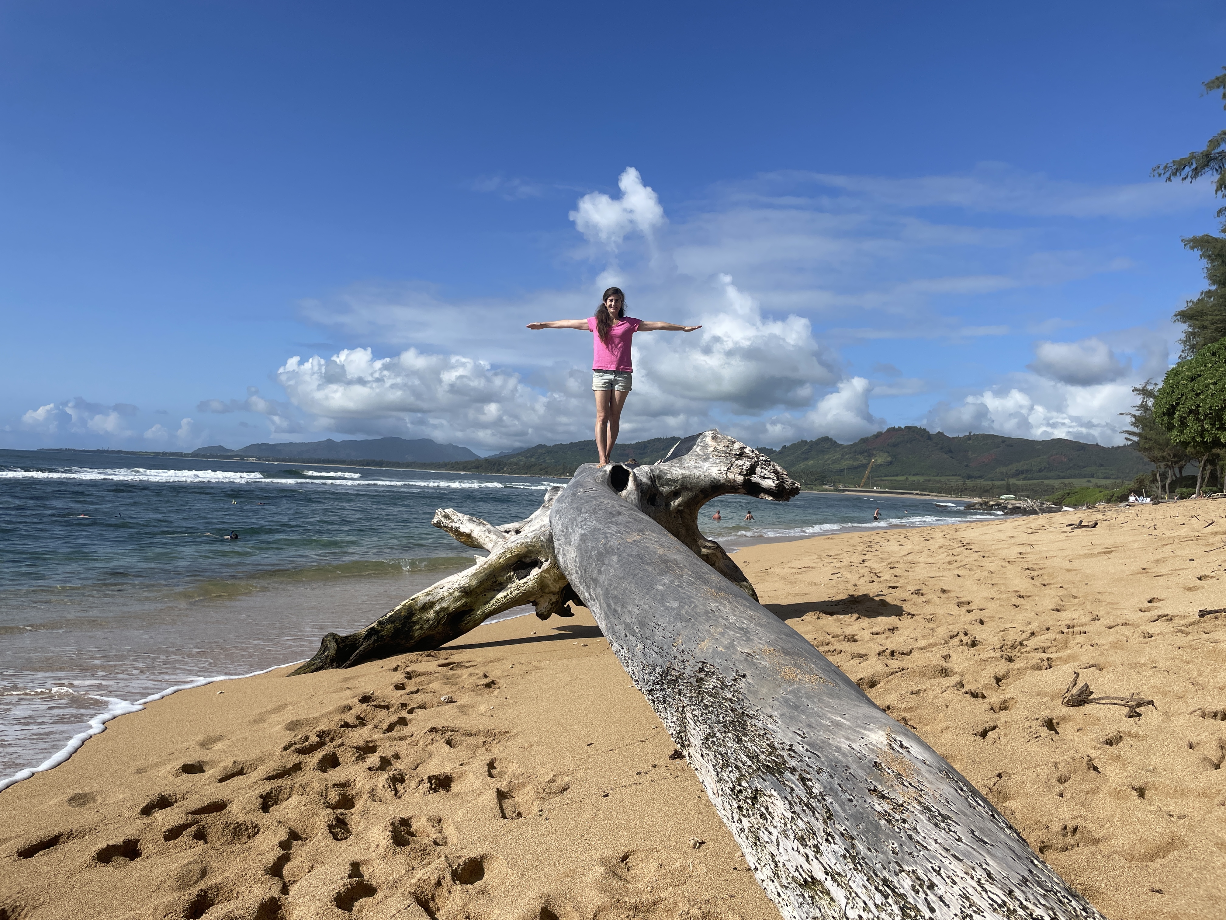 A woman balancing on a driftwood log on a tropical beach