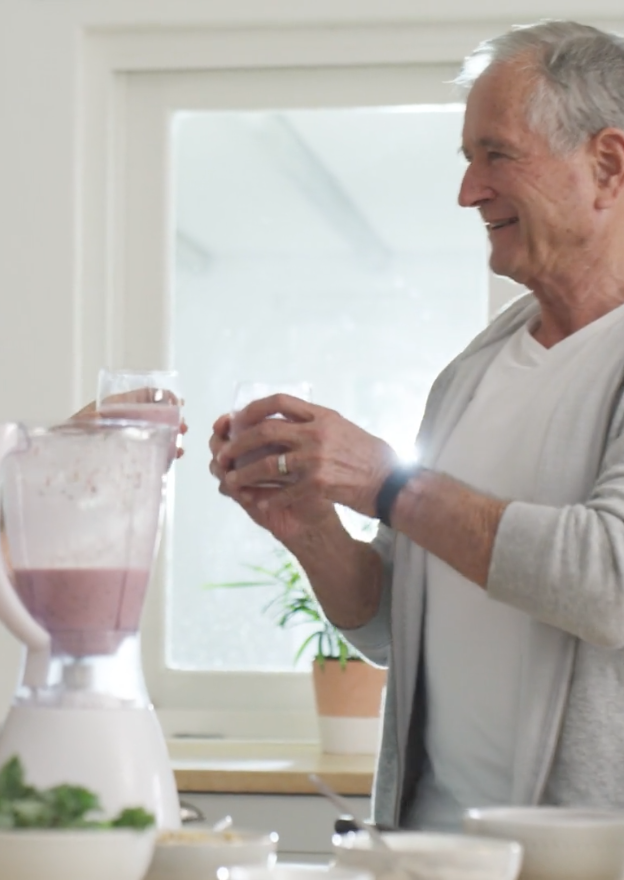 older man making a smoothie and smiling