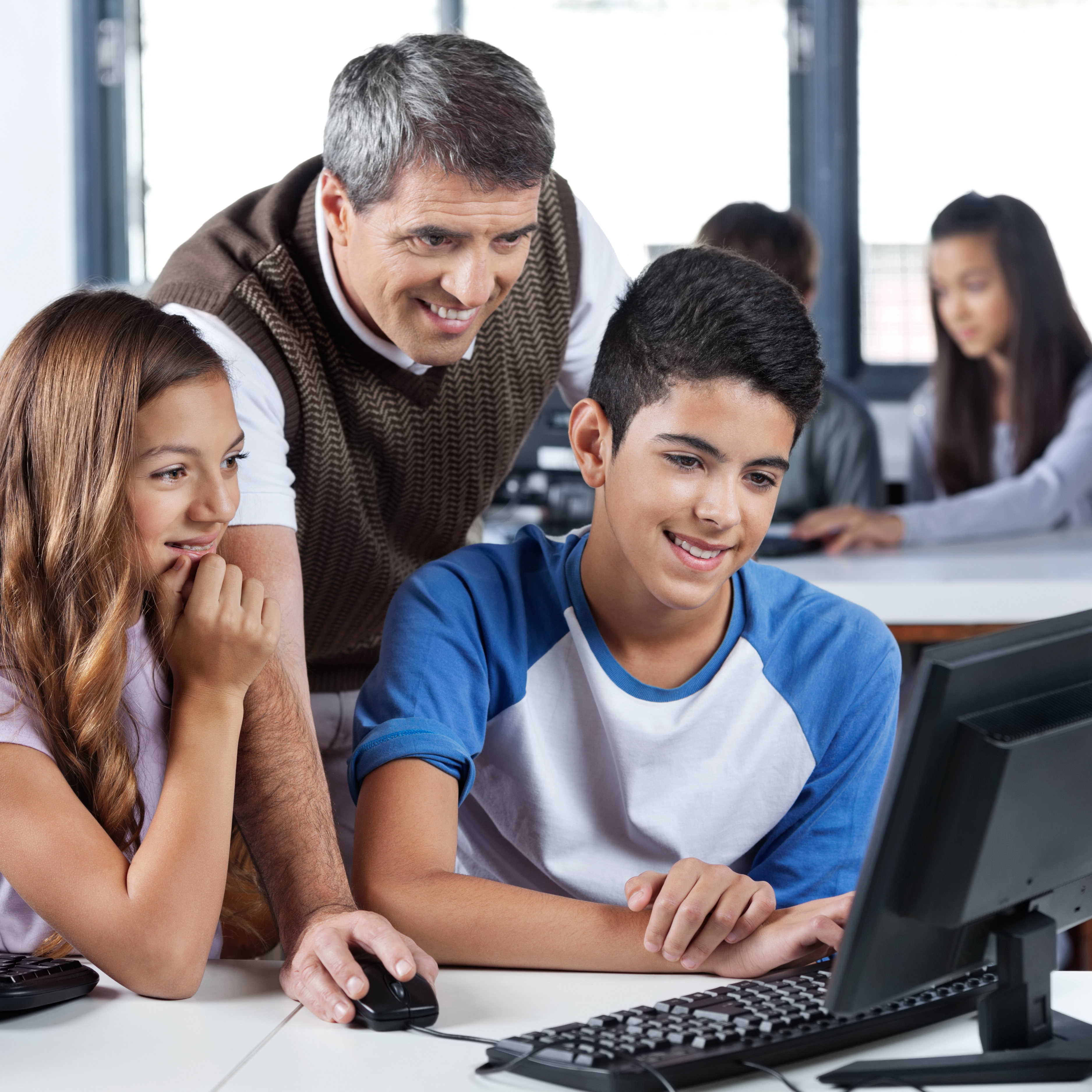 teacher smiling working with students using a computer