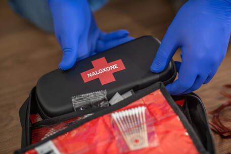 A person wearing blue gloves removing a Naloxone kit from a case, responding to an opioid poisoning emergency as trained by the Canadian Red Cross.