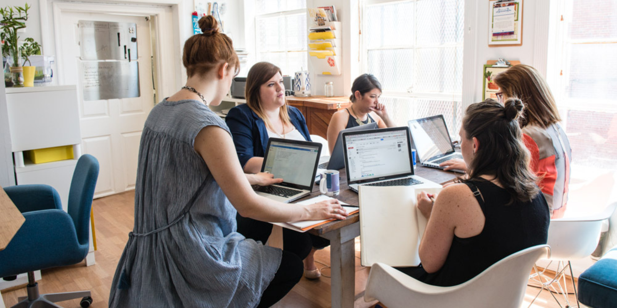 A group of women are sitting around a table at their laptops