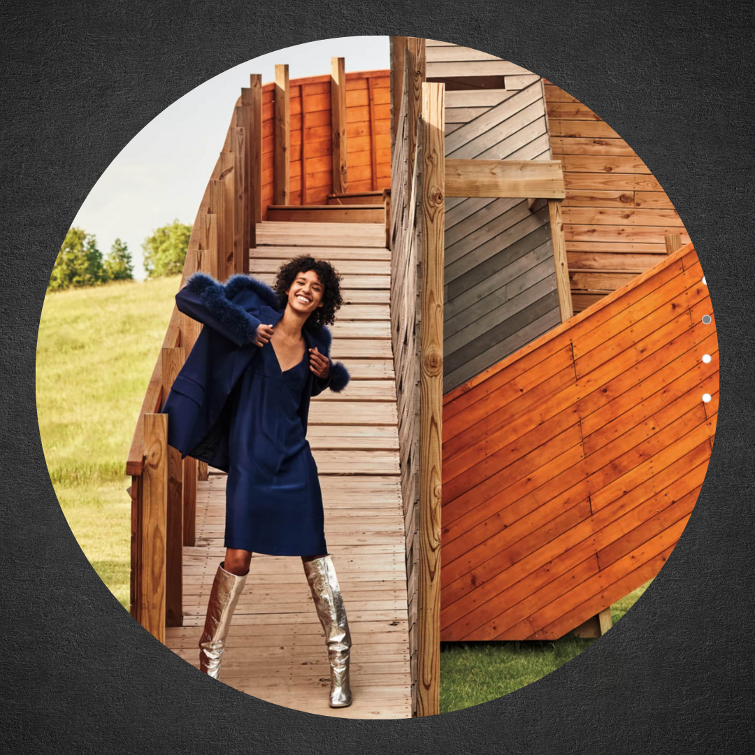 photo of woman in hip clothing and boots putting on jacket in front of modern setting