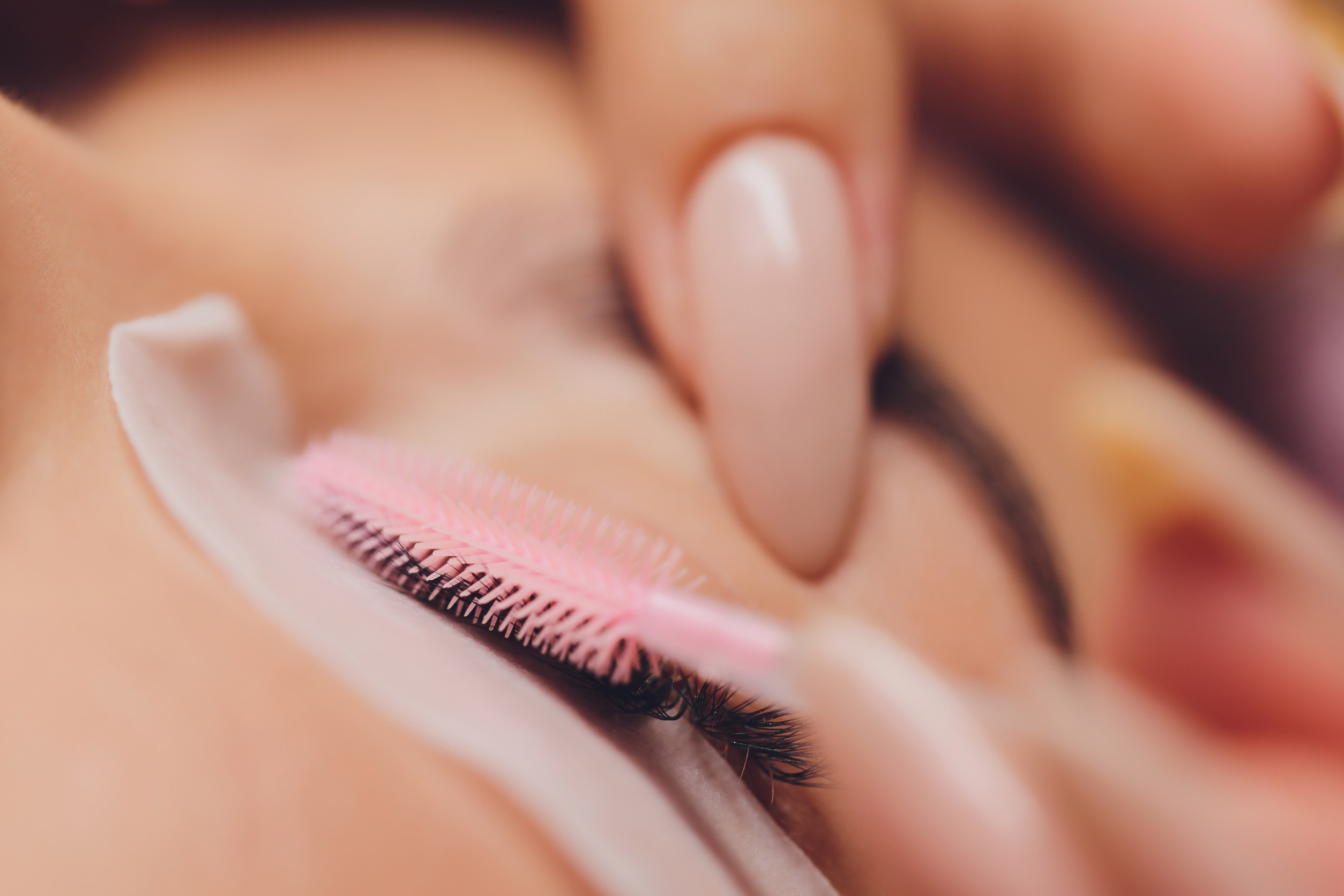 woman brushing eyelash extensions on client with eyes closed and laying down.