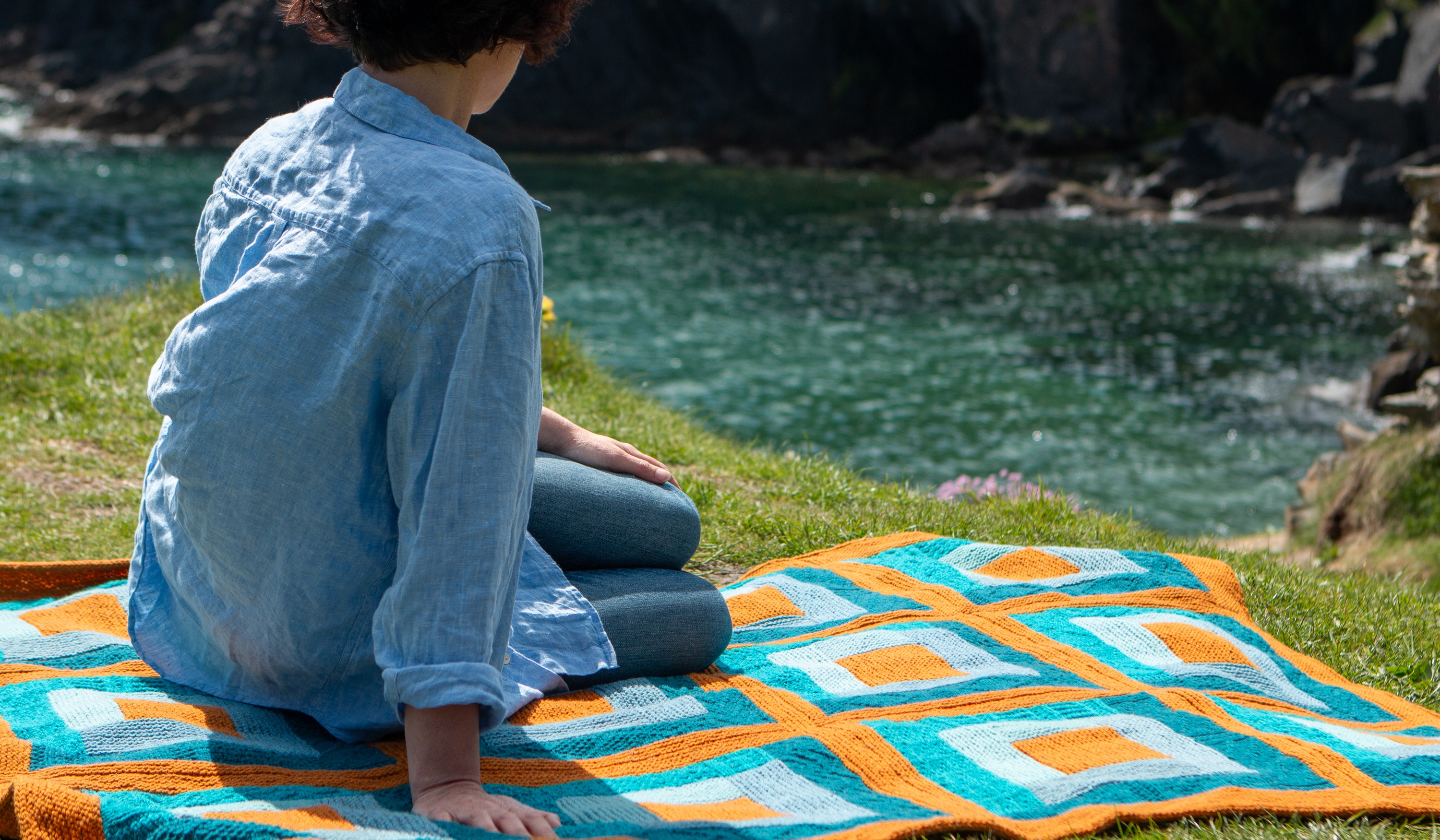 Woman sitting on a colourful blanket looking out at sea.