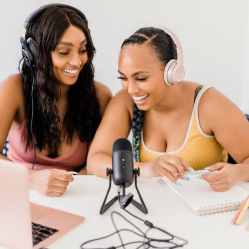 Two podcast hosts recording an episode into a microphone on a desk