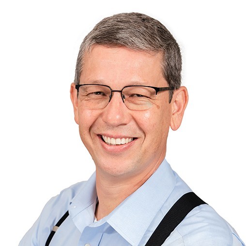 The course instructor smiling at the viewer. Dressed in collar, black suspenders, and black wire-frame glasses.