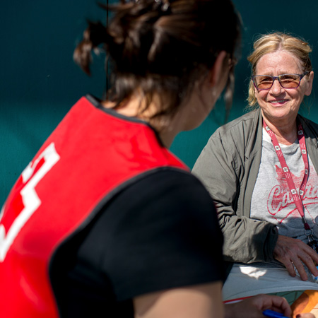 A person wearing a Canadian Red Cross vest talking to another person who is smiling, all happening on a sunny day.