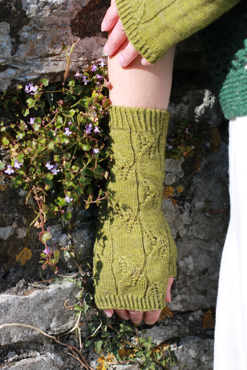 green cable and lace handknit mitts photragphed against and old stone wall 