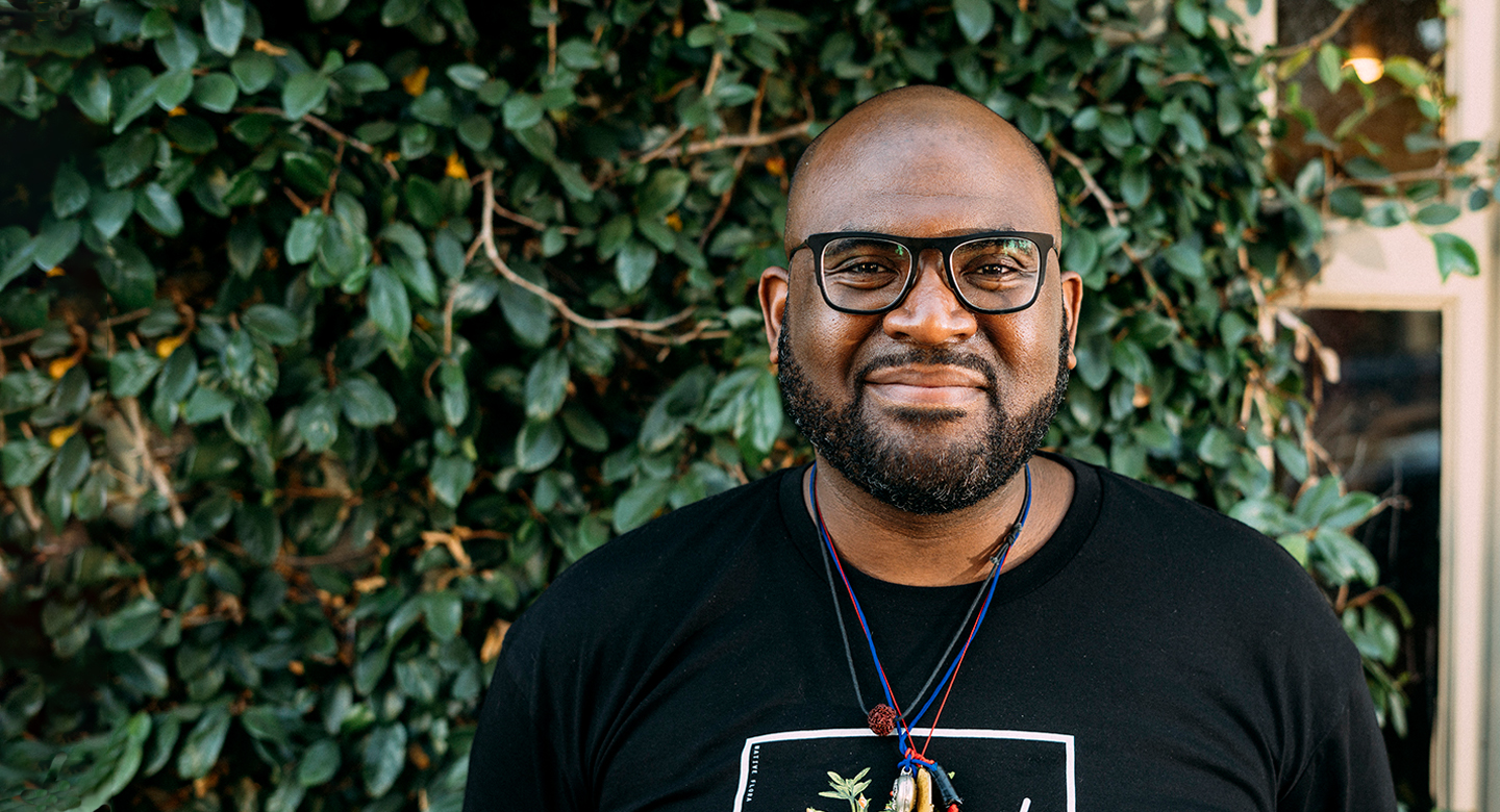 A photo of Lama Rod Owens in front of a wall with buddhas painted on it