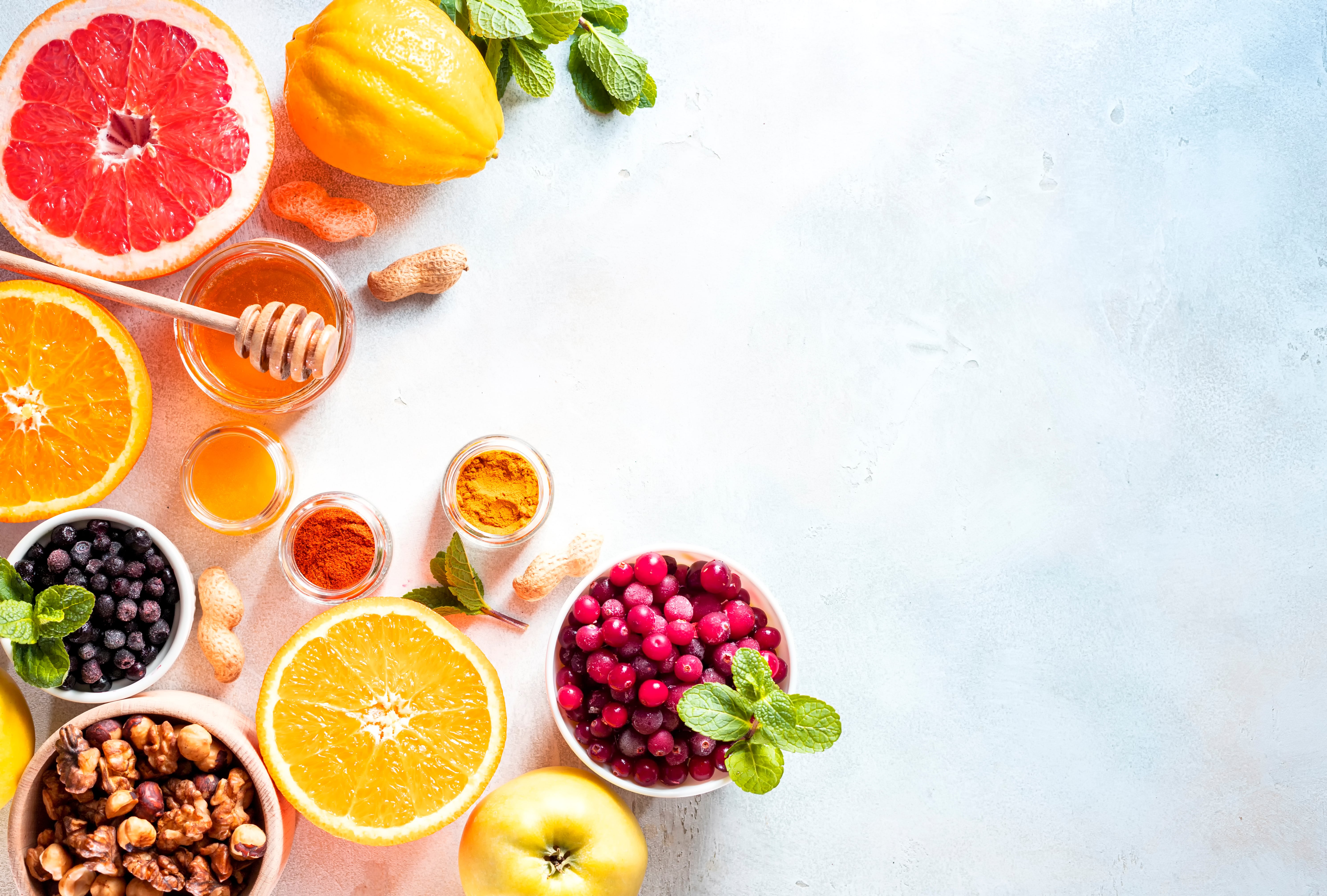 flat lay of citrus, cranberries, nuts, berries, honey, turmeric powders on a white background