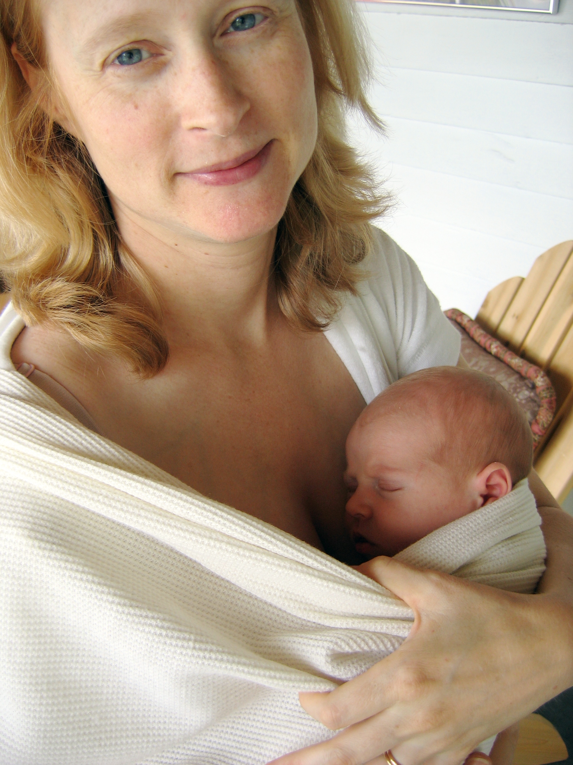 peaceful mother holding newborn baby in white fabric wrap