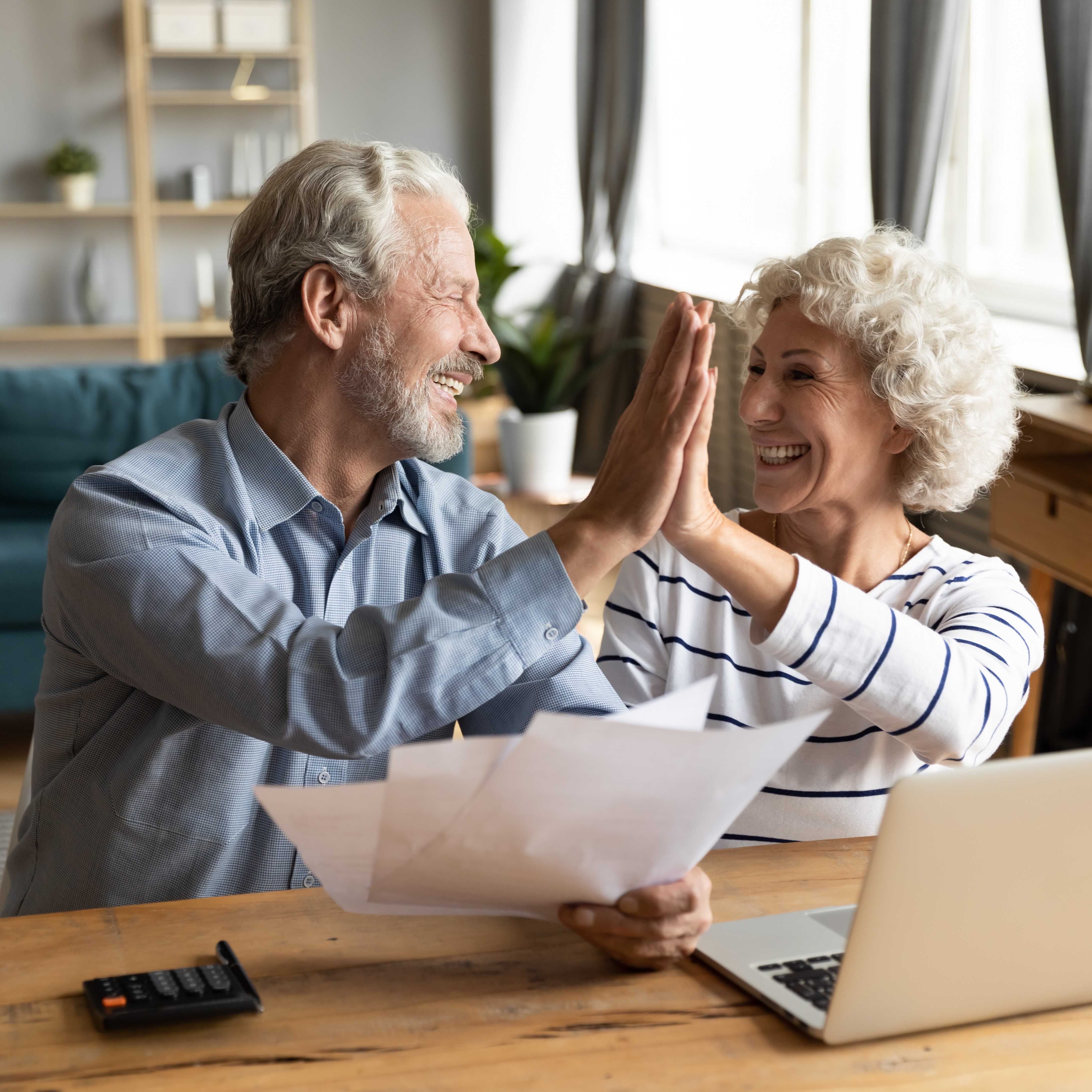 Retired couple high-fiving with a laptop and papers