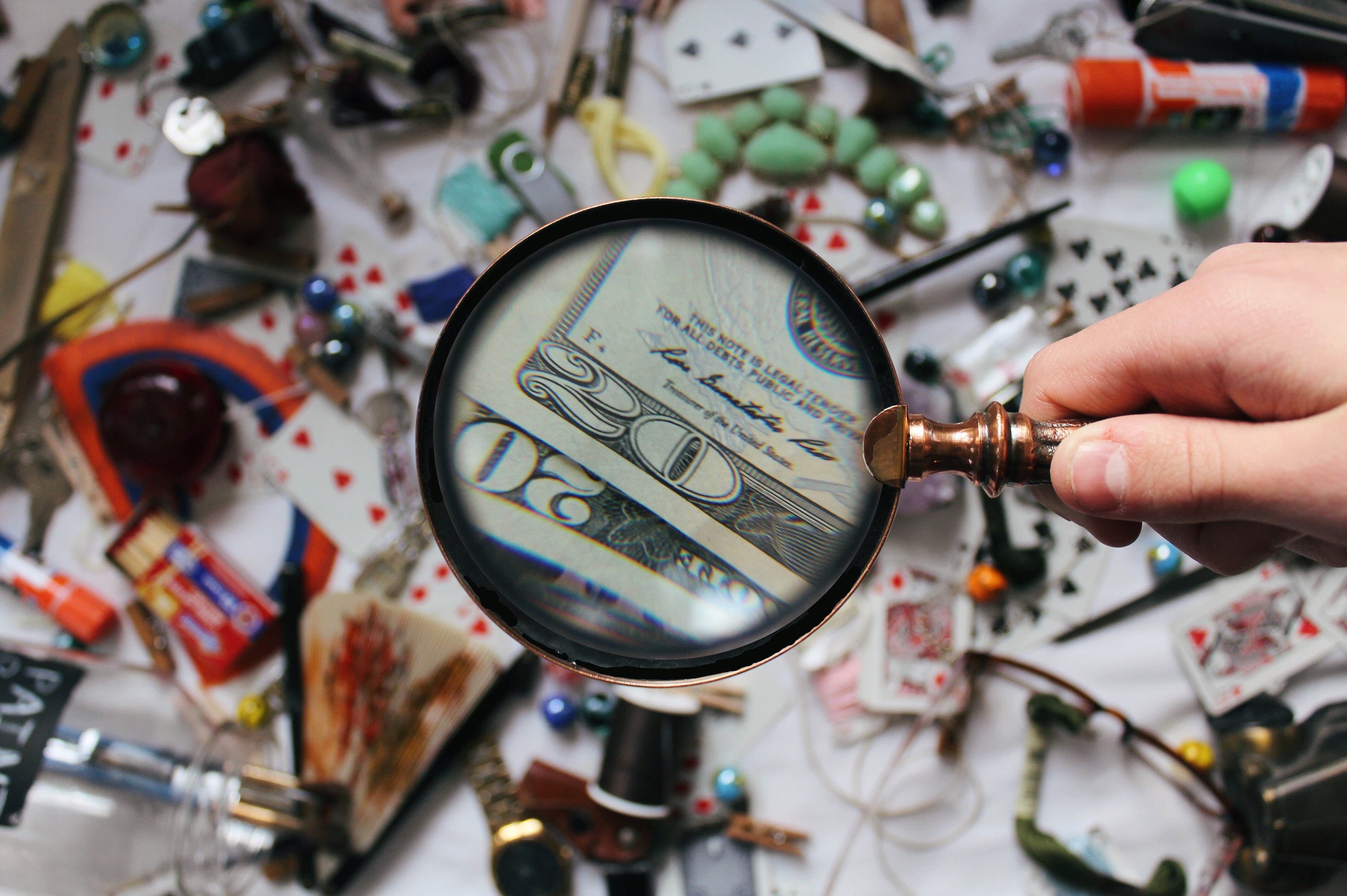 Person holding magnifying glass over a collection of items with two $20 bills in focus