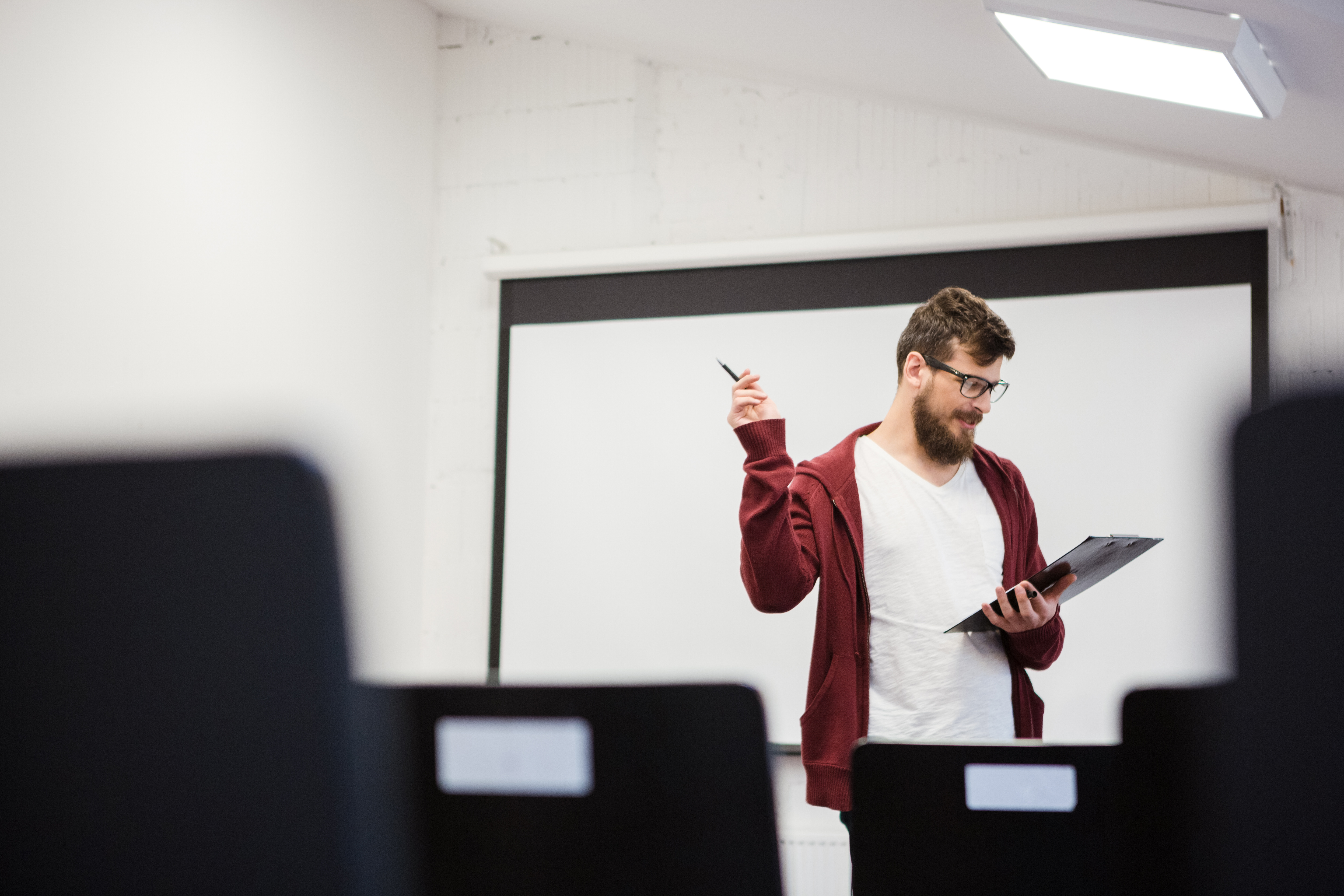 A male teacher stands in a computer lab looking down at a clipboard