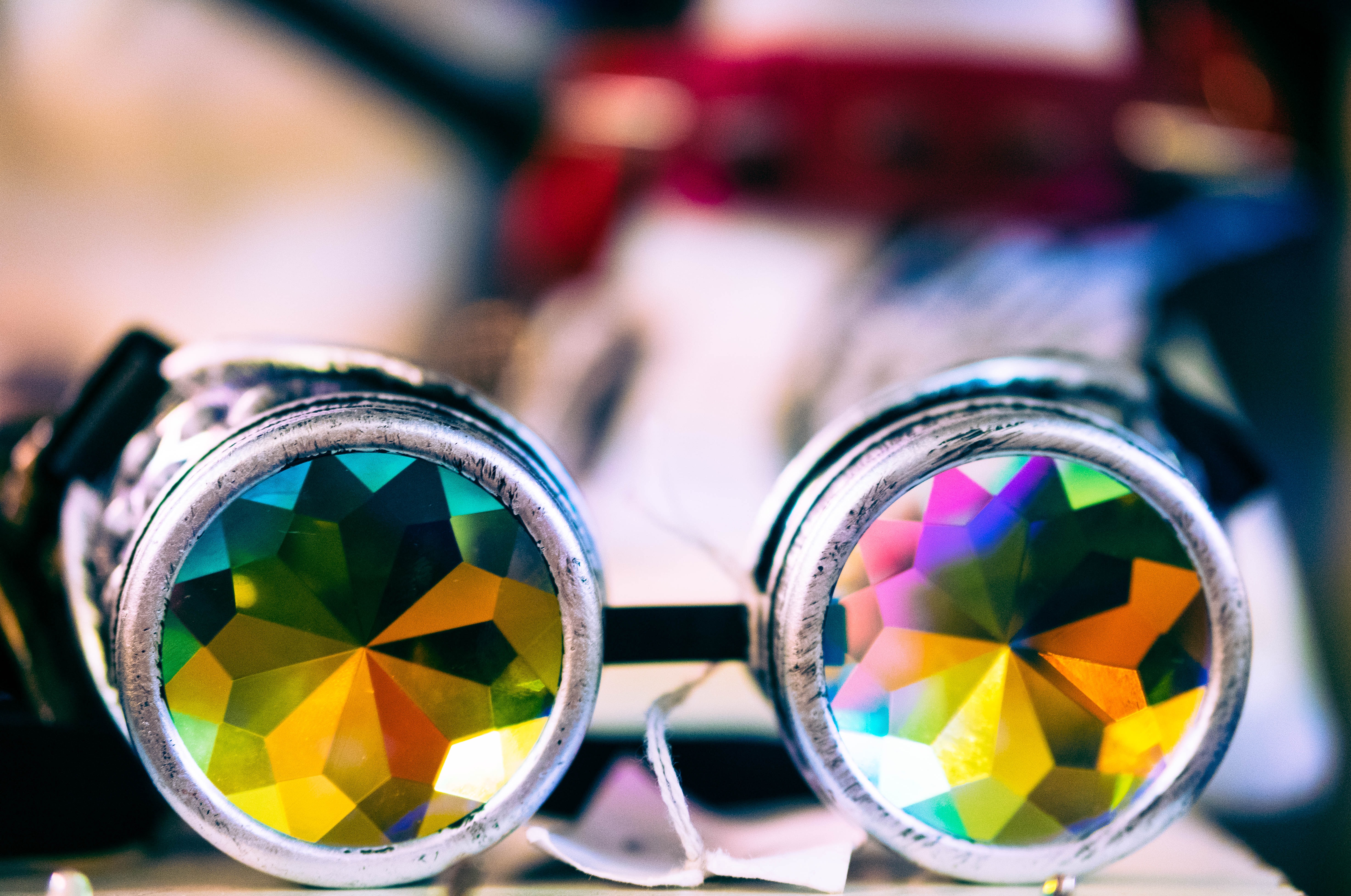 An image of a kaleidescope with silver rims, multi color fractals on the lenses and a blurred background