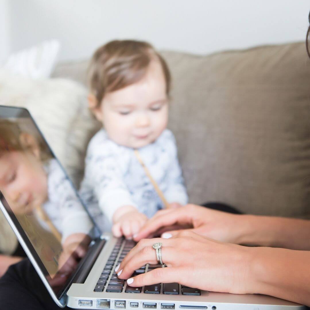 woman working on computer with a baby in the background