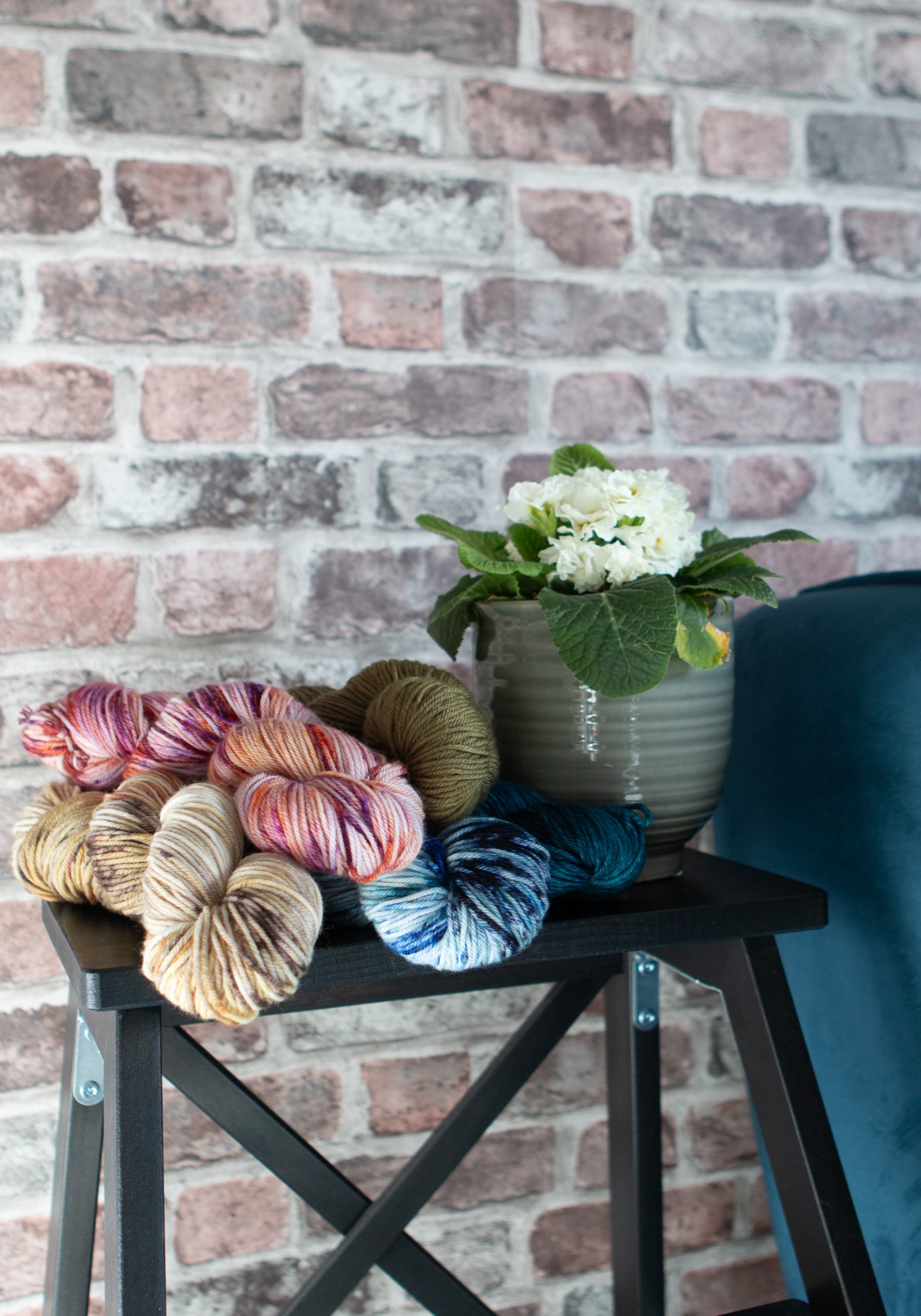 All of the yarn options pilled on a stool with a folwer pot next to them.