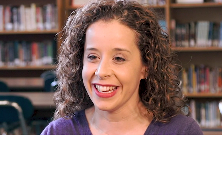 Educator smiling in a library during an interview.