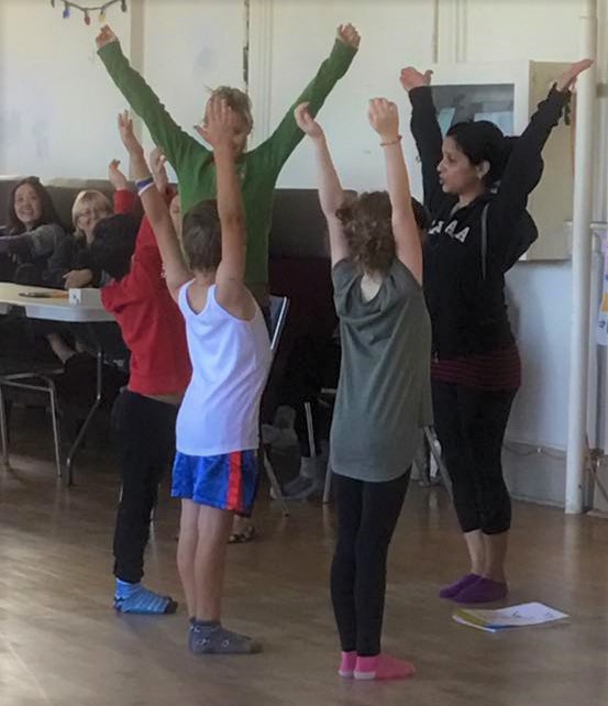 Kids Yoga Teacher Training Scavenger Hunt Game With Teacher leading children in the upward hands yoga pose  