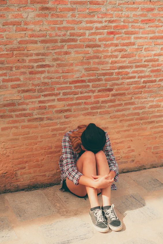 A teenager sitting alone on brick wall with head down on knees